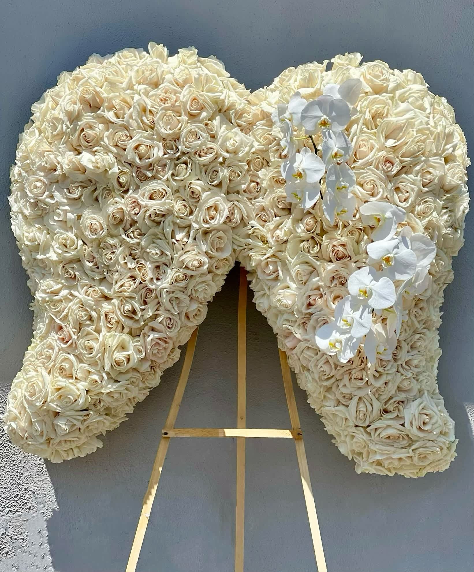 Heart-shaped floral tribute of cream roses with white orchids on an easel