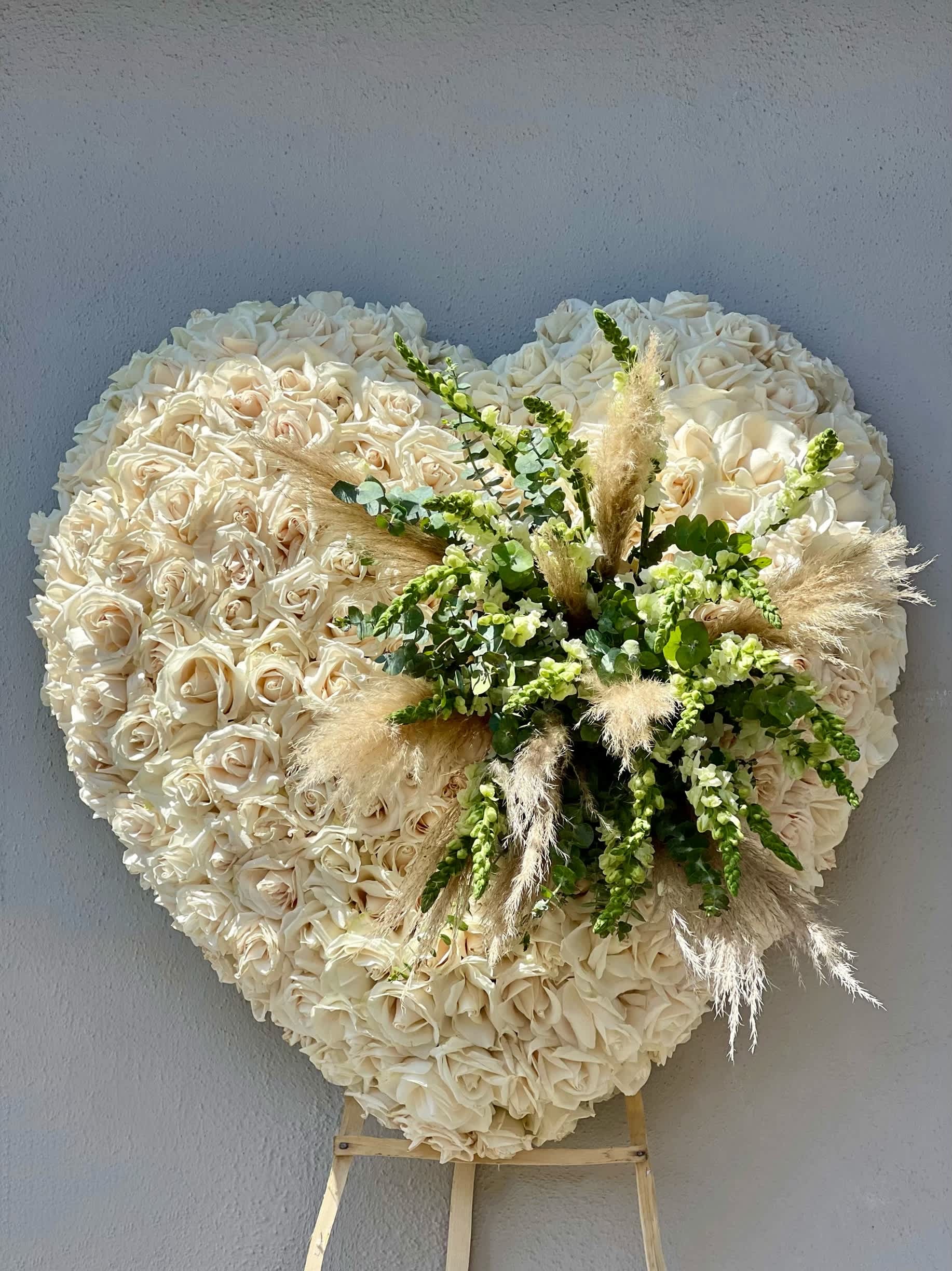 Heart-shaped cream rose floral display with greenery and pampas grass
