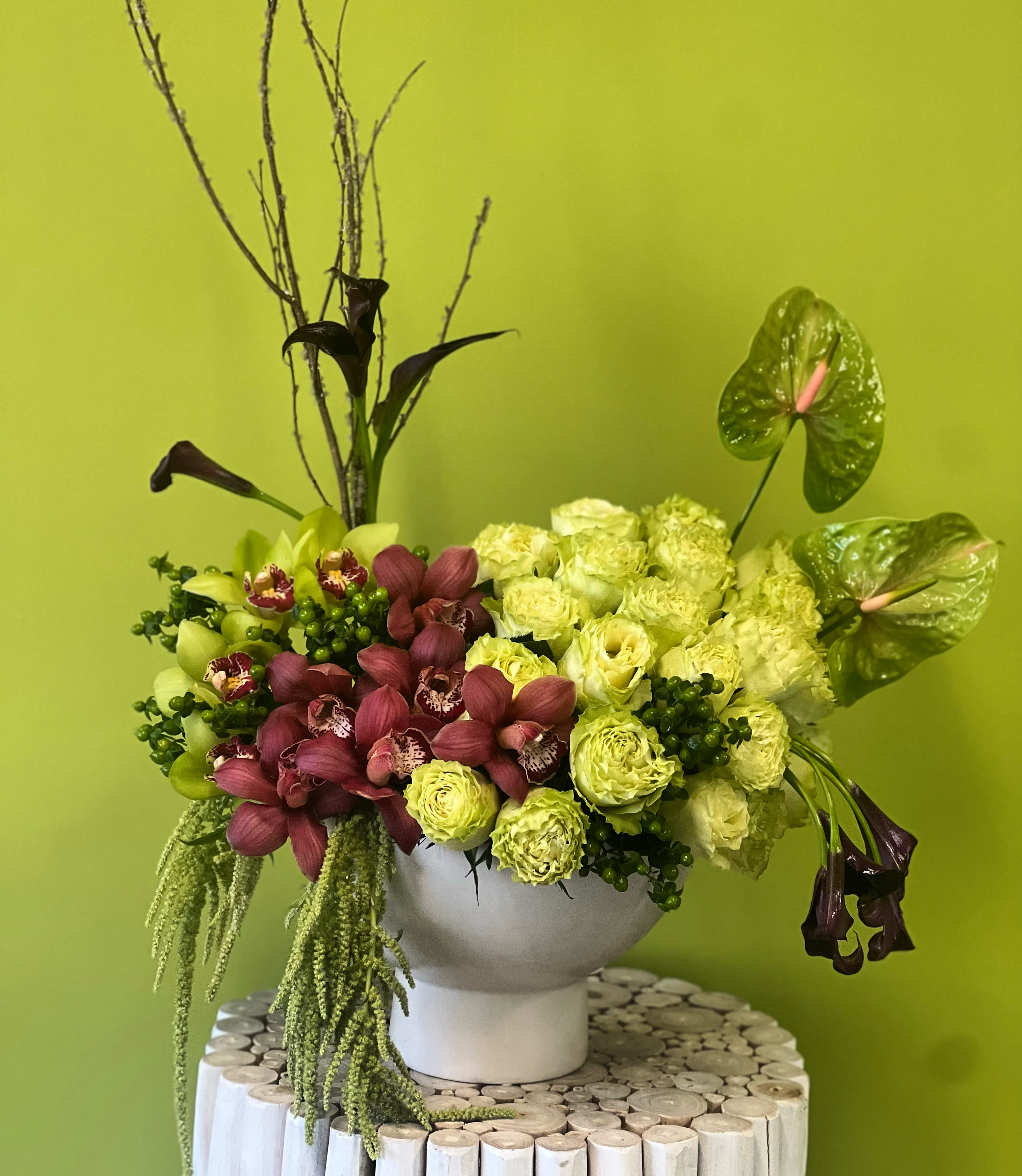 Floral arrangement with green and burgundy orchids in a white vase