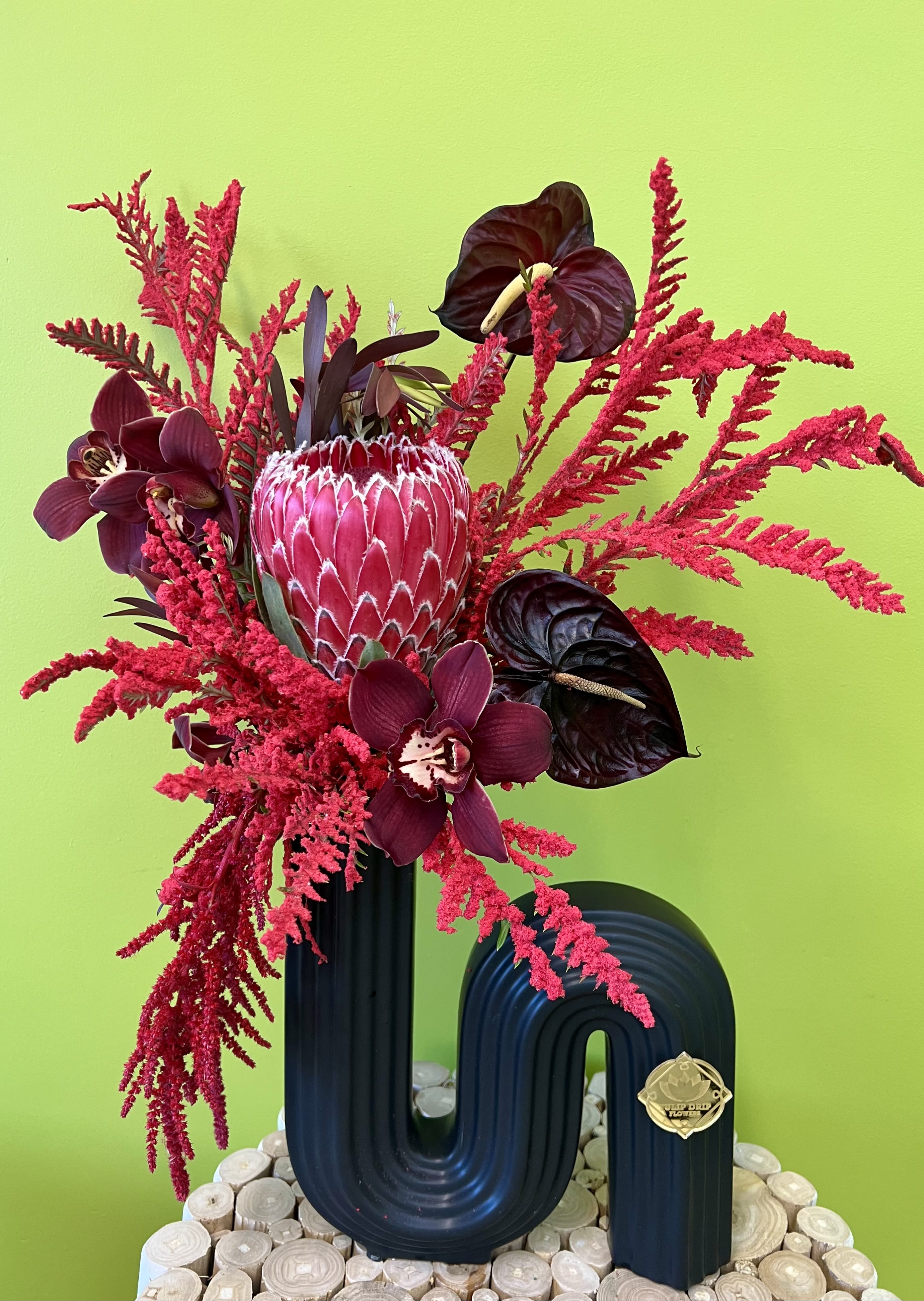 Bold red floral arrangement with orchids and a protea in a black vase
