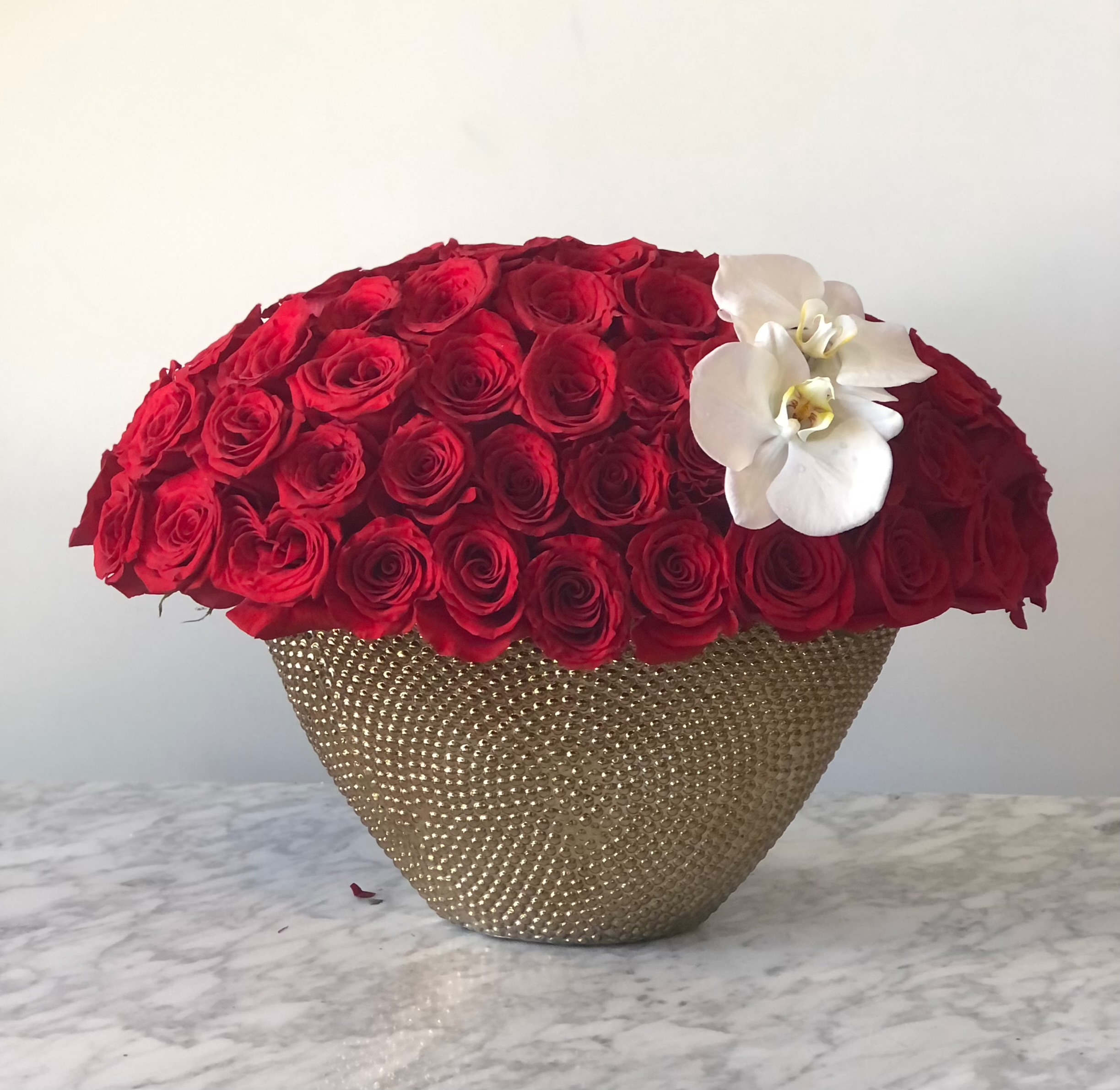 Red rose arrangement in a gold textured vase with white orchids