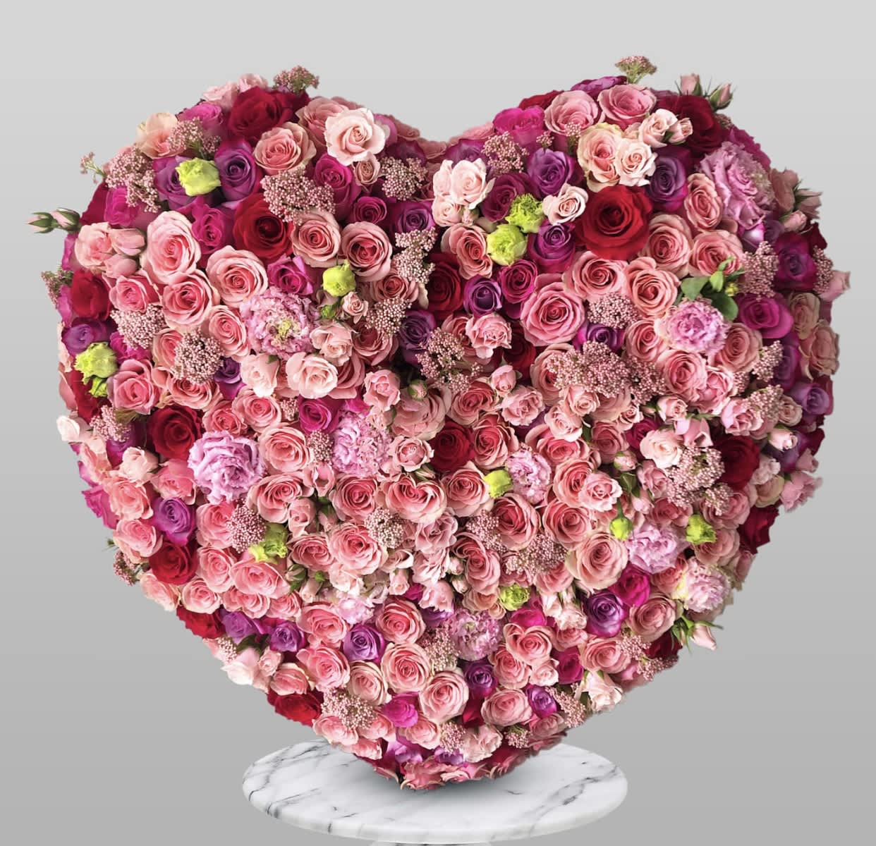 Heart-shaped arrangement of pink and red roses on a marble stand