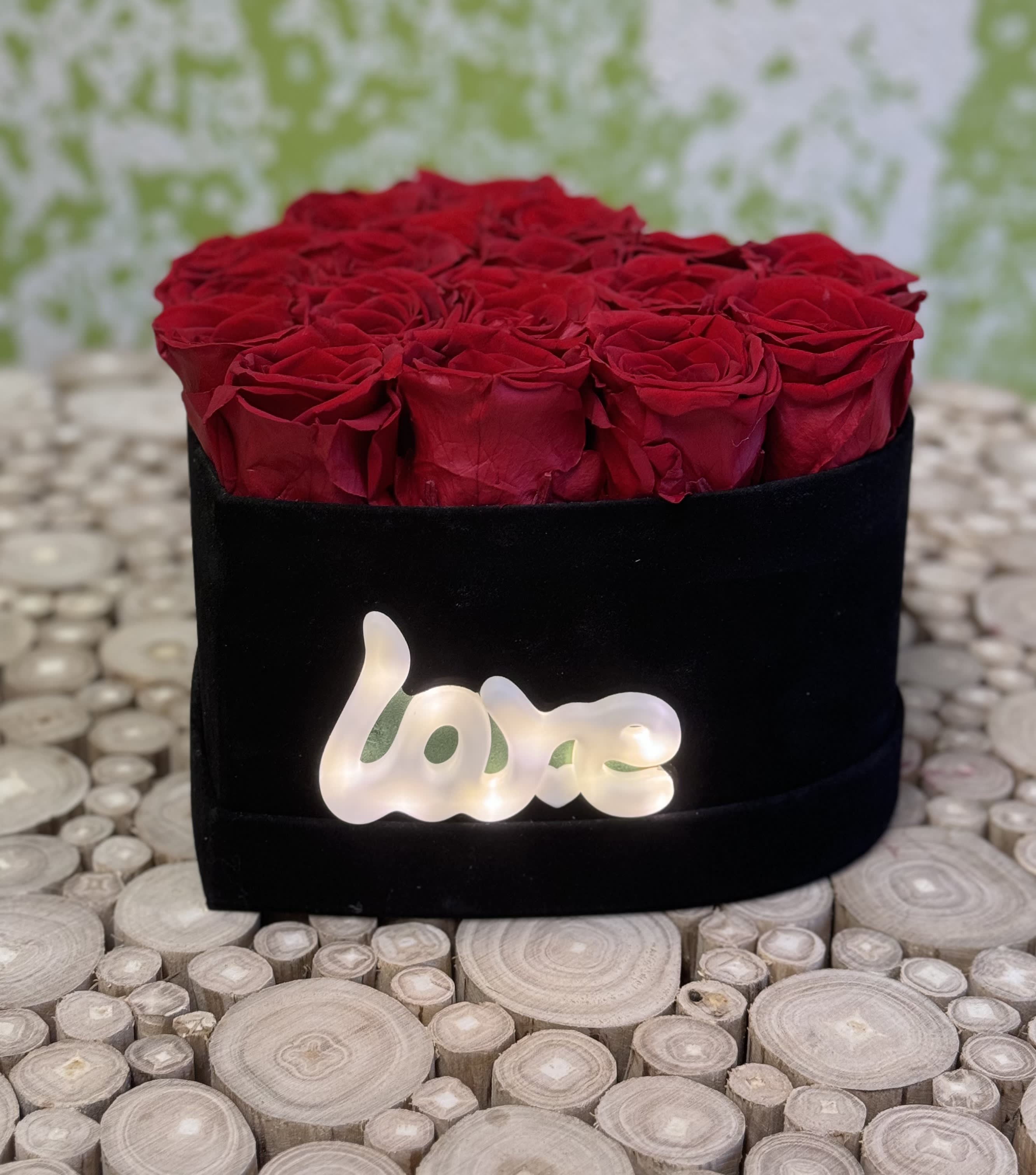 Red roses arranged in a black box with a glowing "love" sign