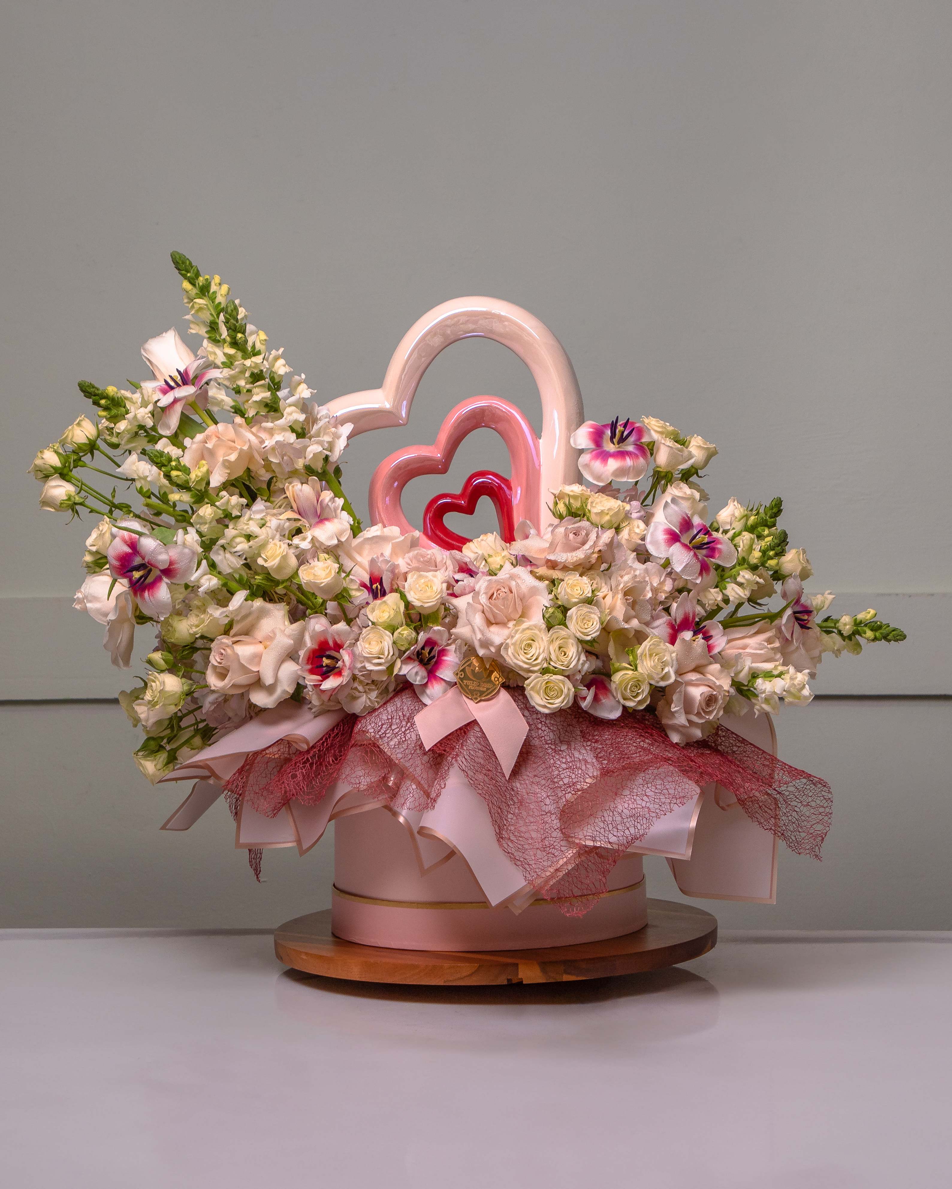 Pink and white floral arrangement in a round box with heart decorations