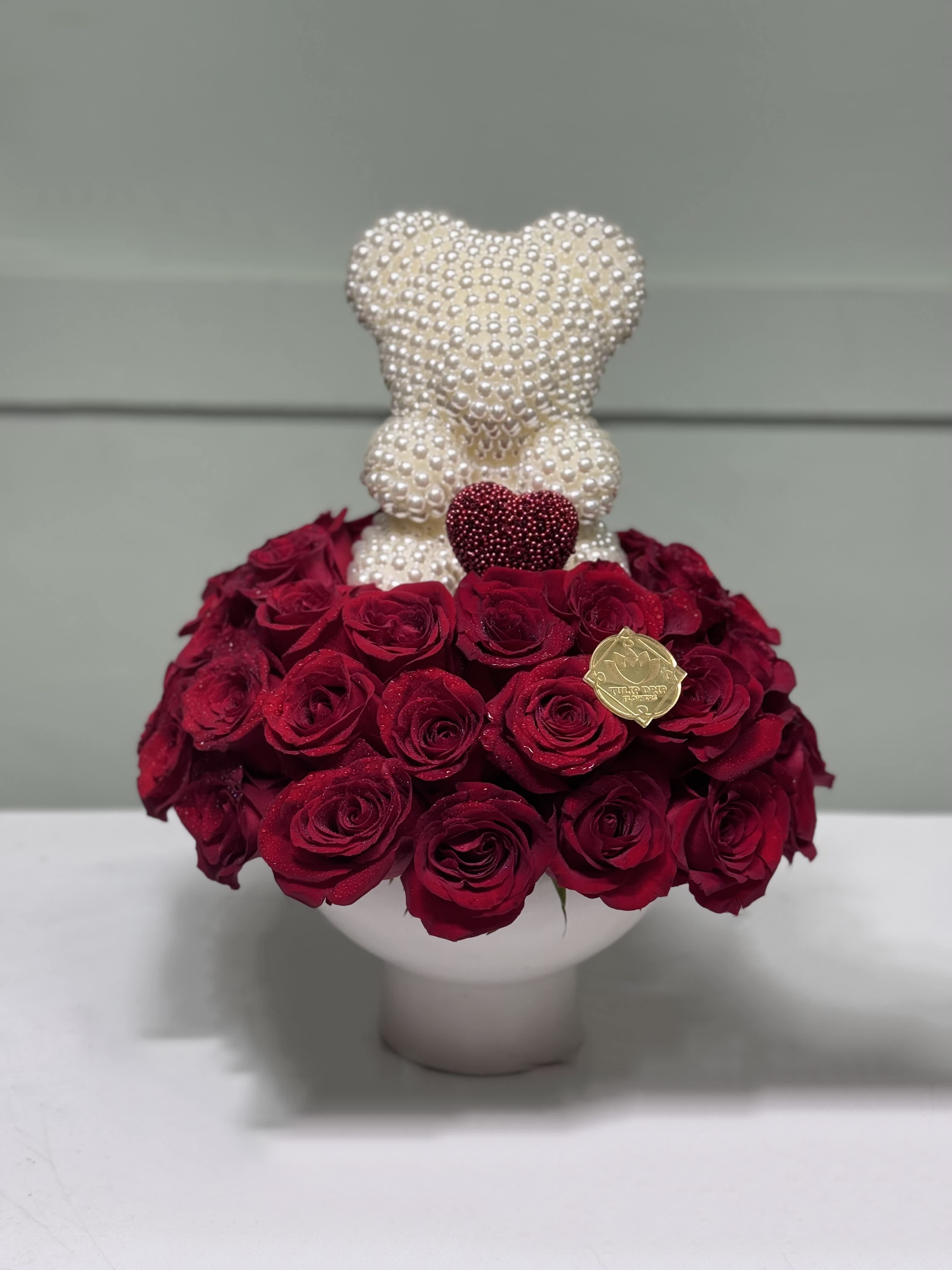 Red rose arrangement with a pearl teddy bear topper in a white vase