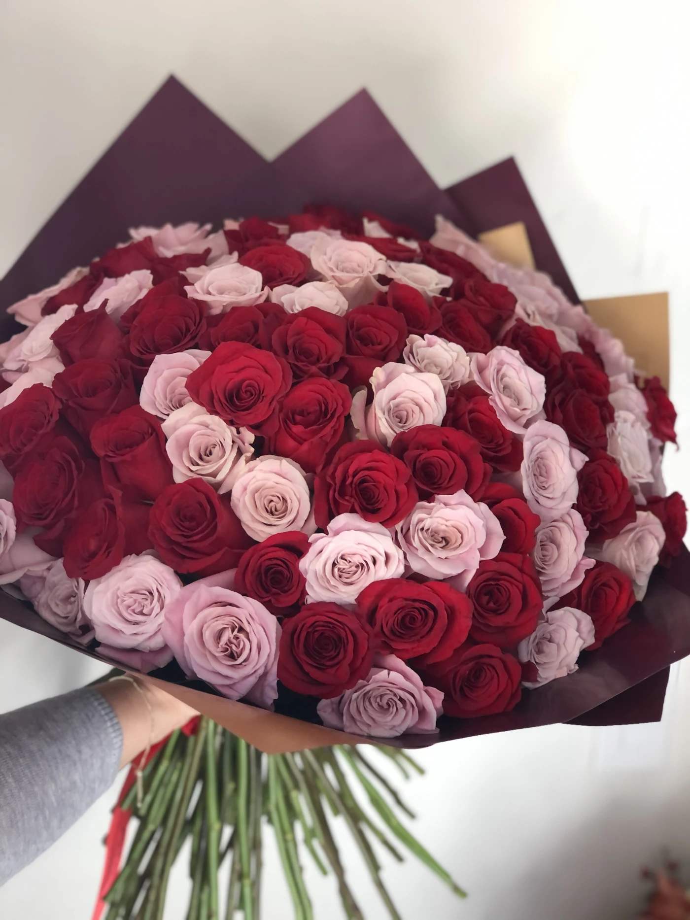 Large bouquet of red and pale pink roses wrapped in dark paper