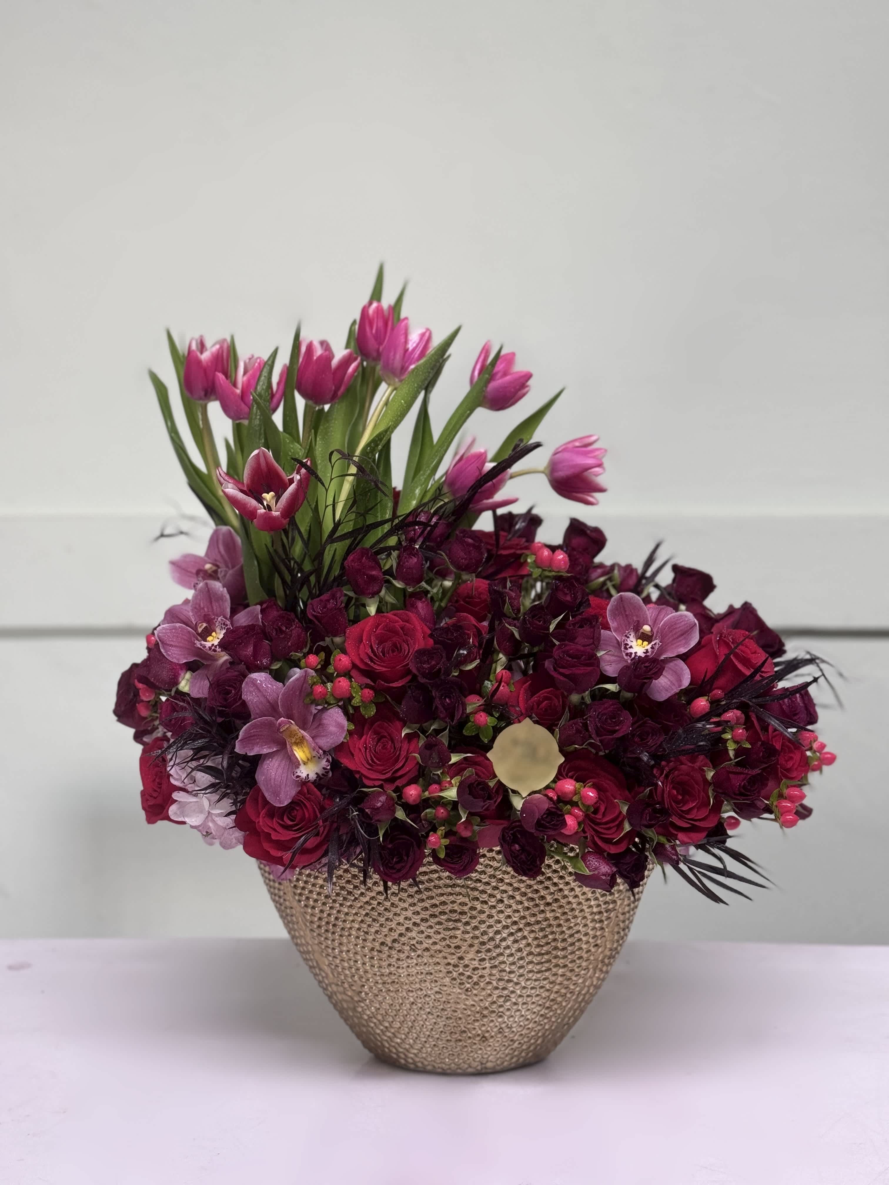Pink tulips and roses arranged in a textured gold vase