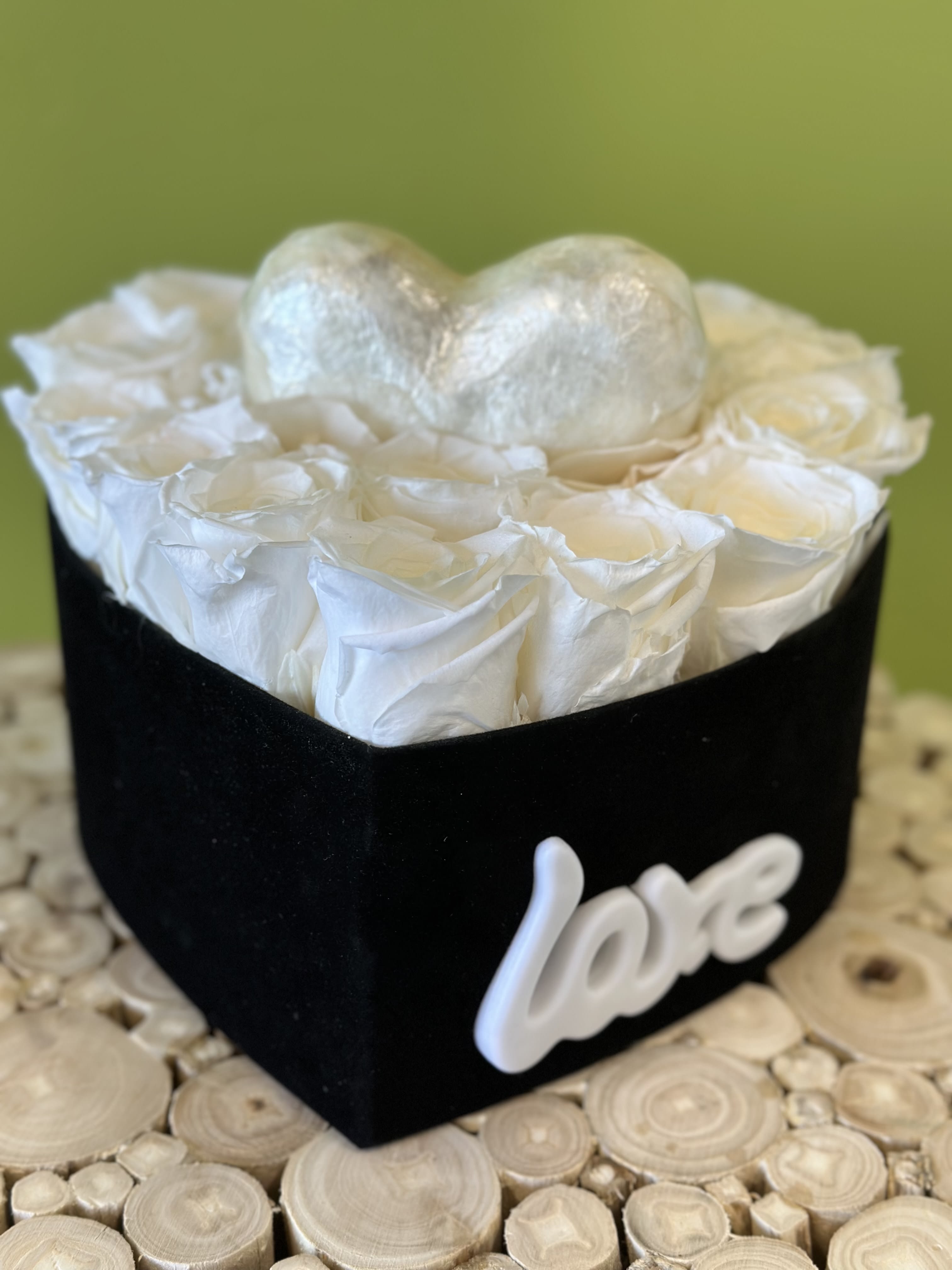 White roses in a black heart-shaped box with a silver heart topper