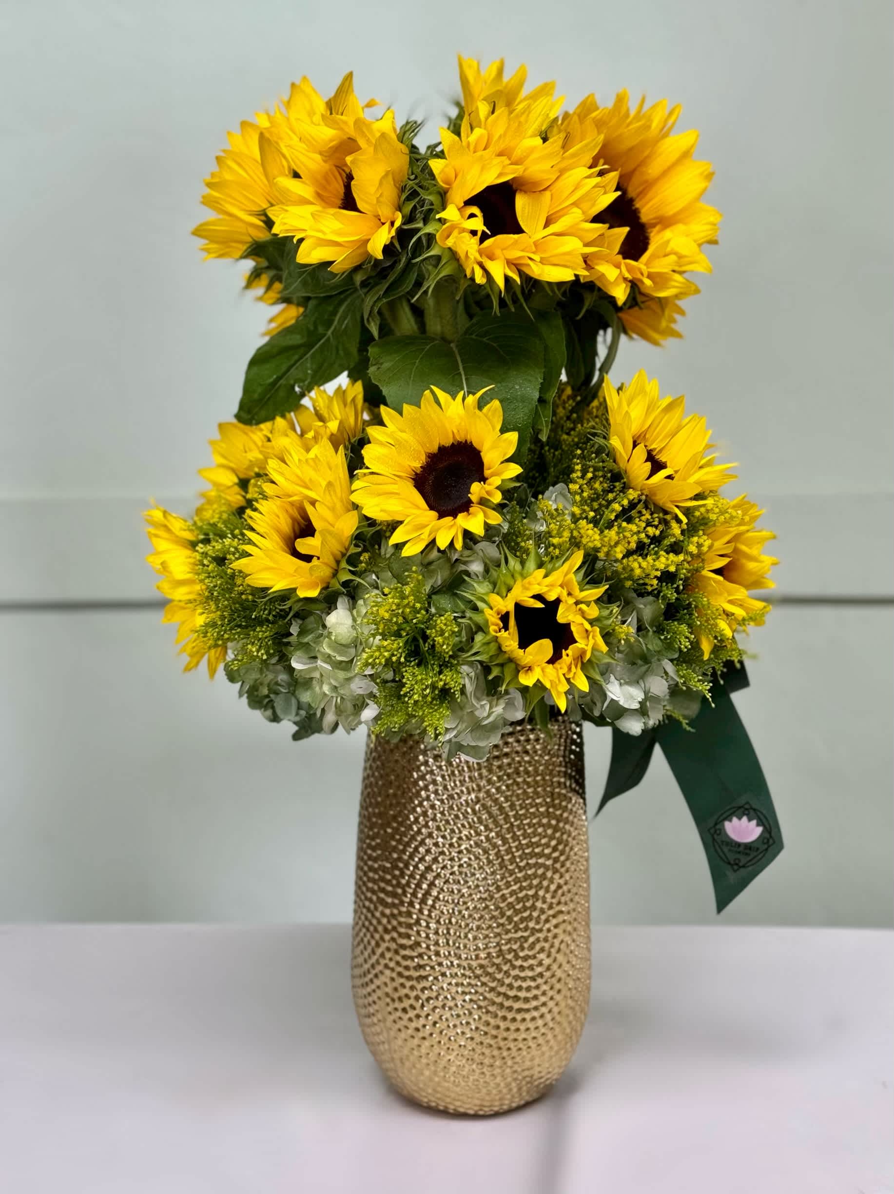 Sunflower arrangement in a gold textured vase with a green ribbon