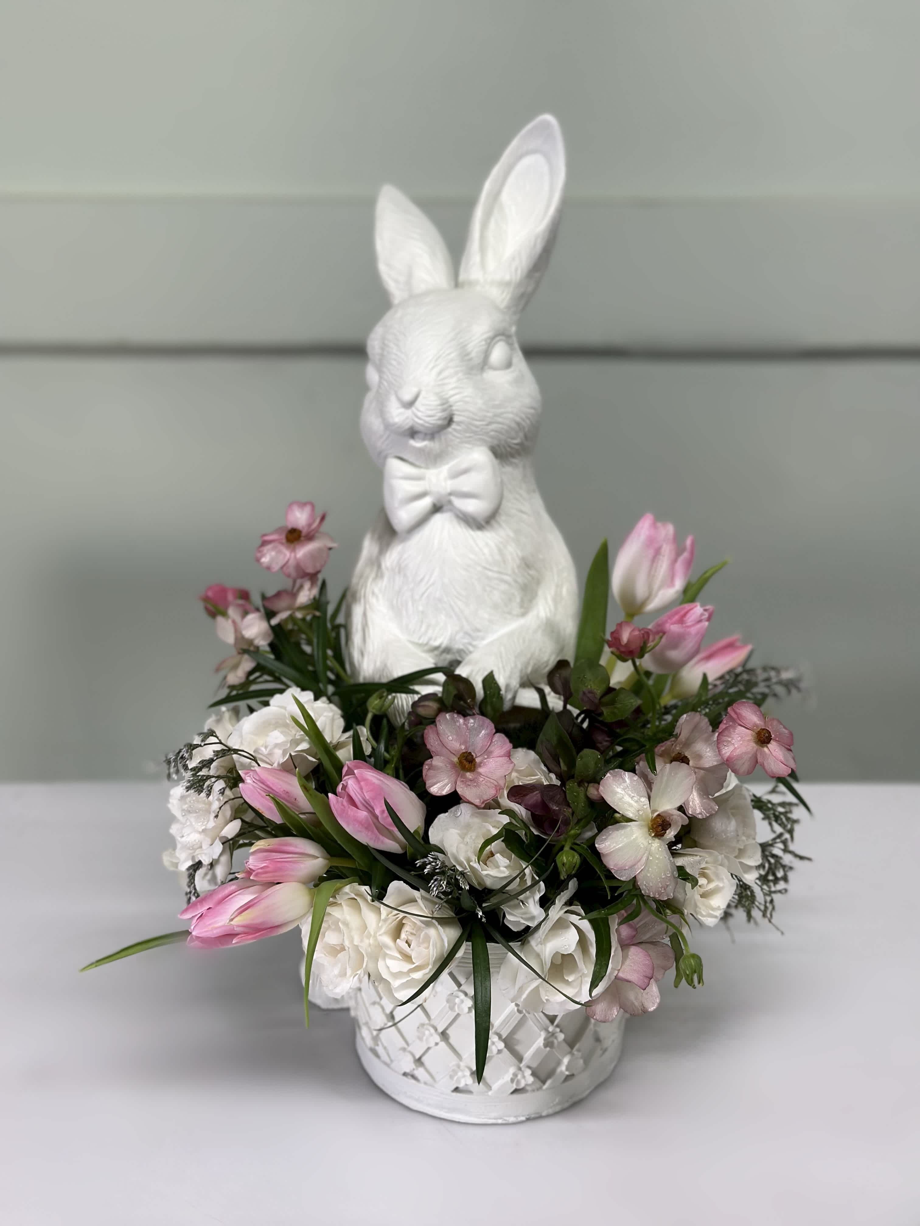 White bunny figurine in a flower basket with pink and white tulips