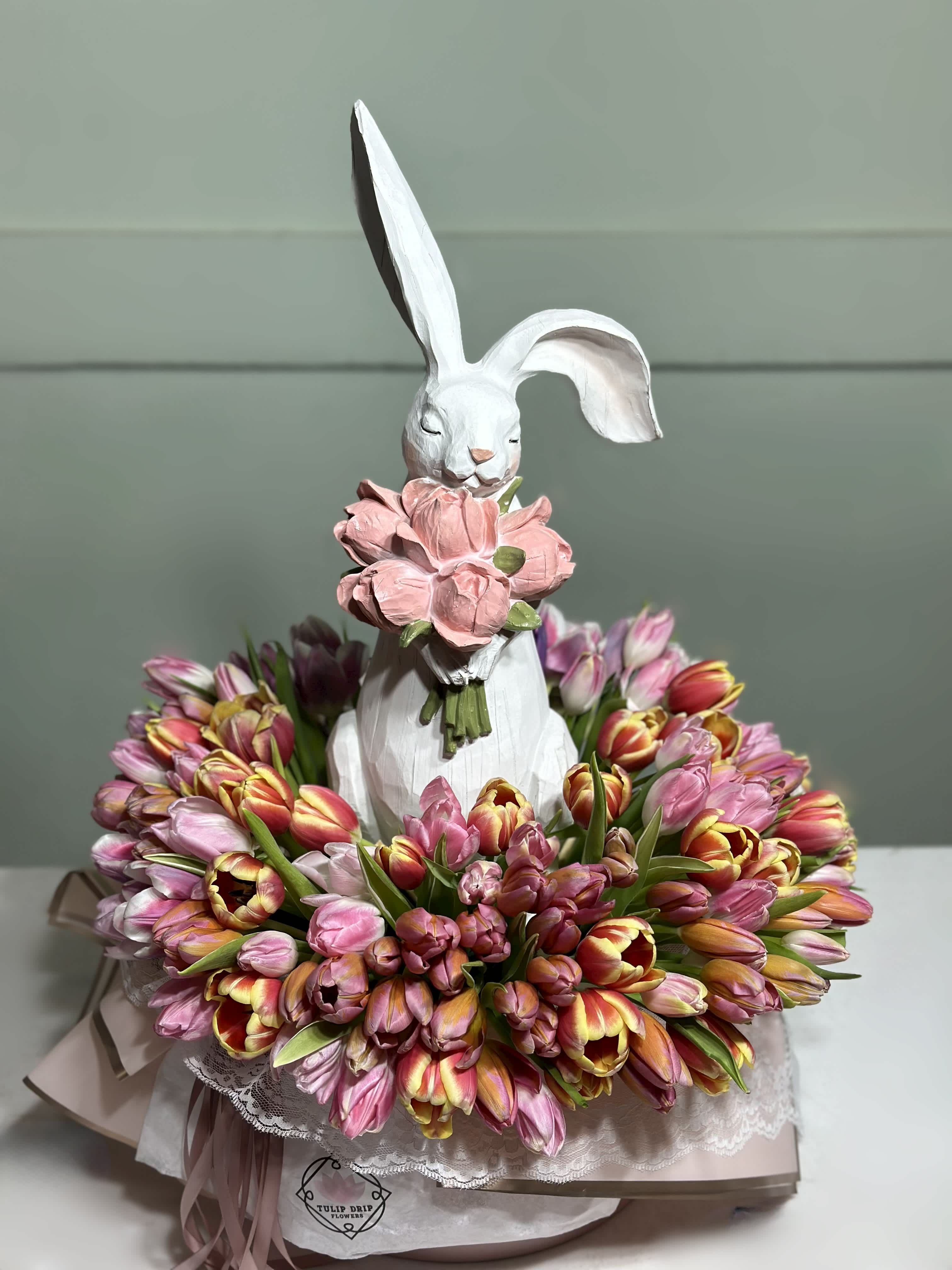 White rabbit figurine holding pink flowers, surrounded by a ring of pink and yellow tulips