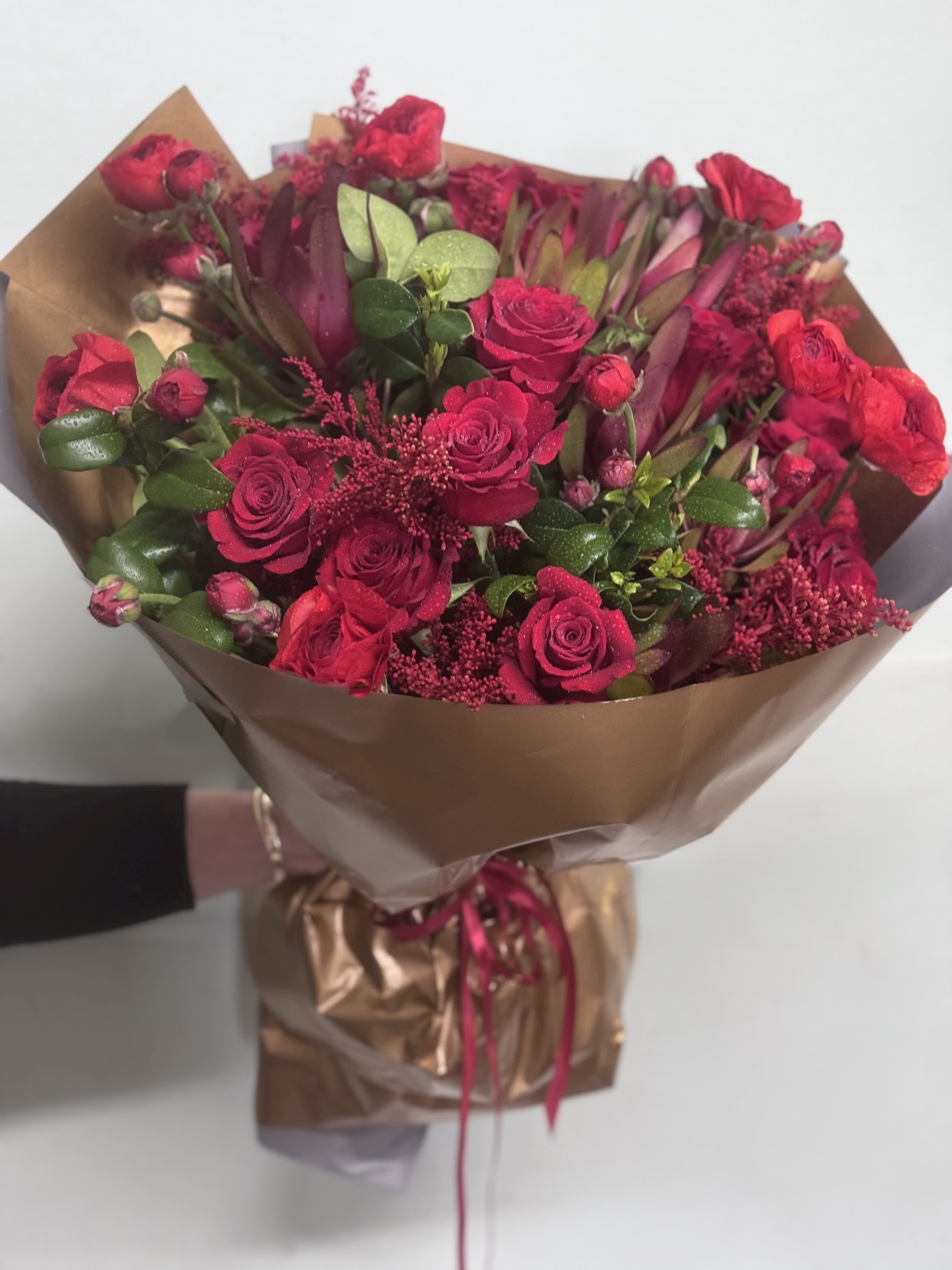 Bouquet of red roses and burgundy flowers wrapped in brown paper