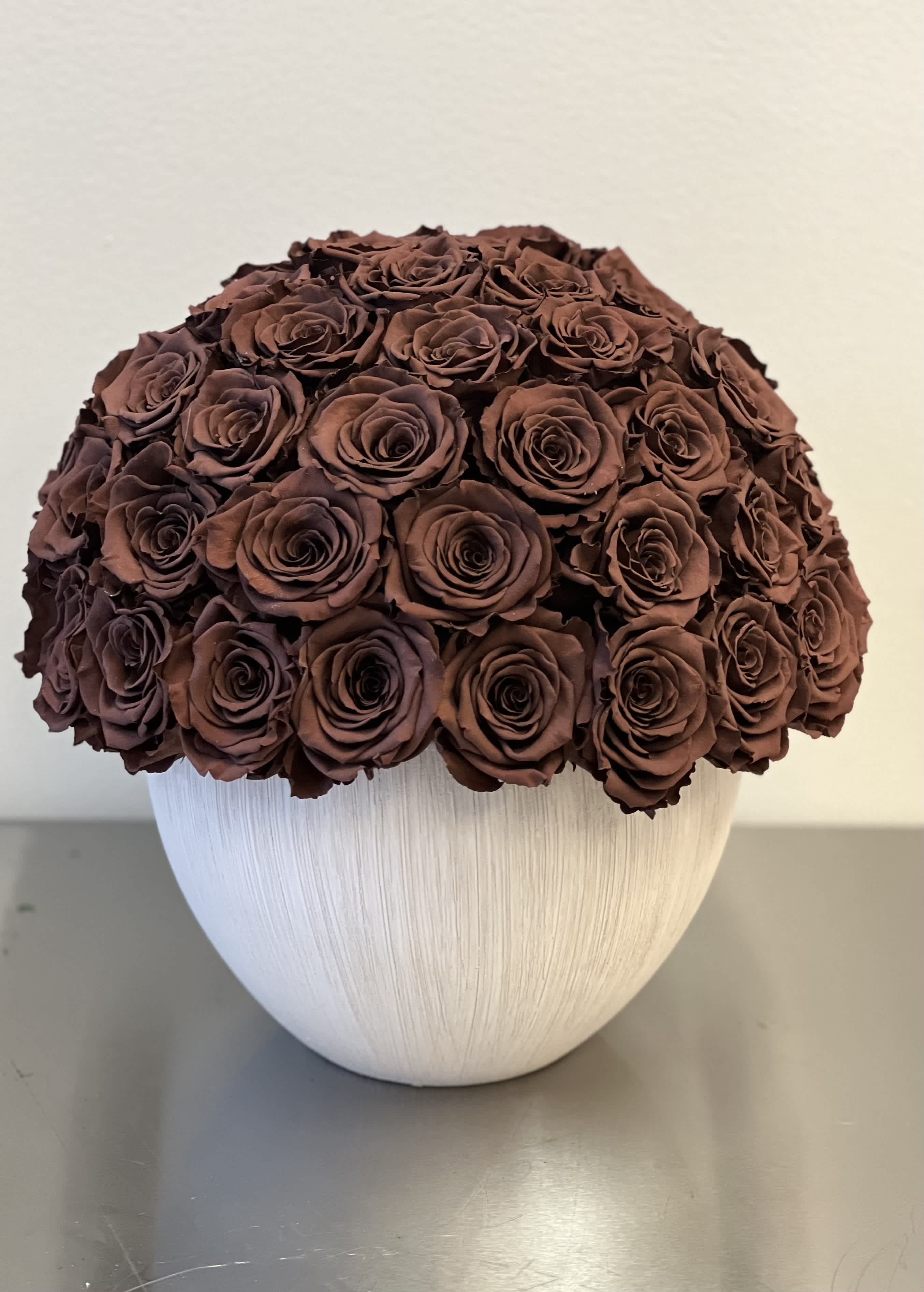 Round bouquet of dark brown roses in a white vase