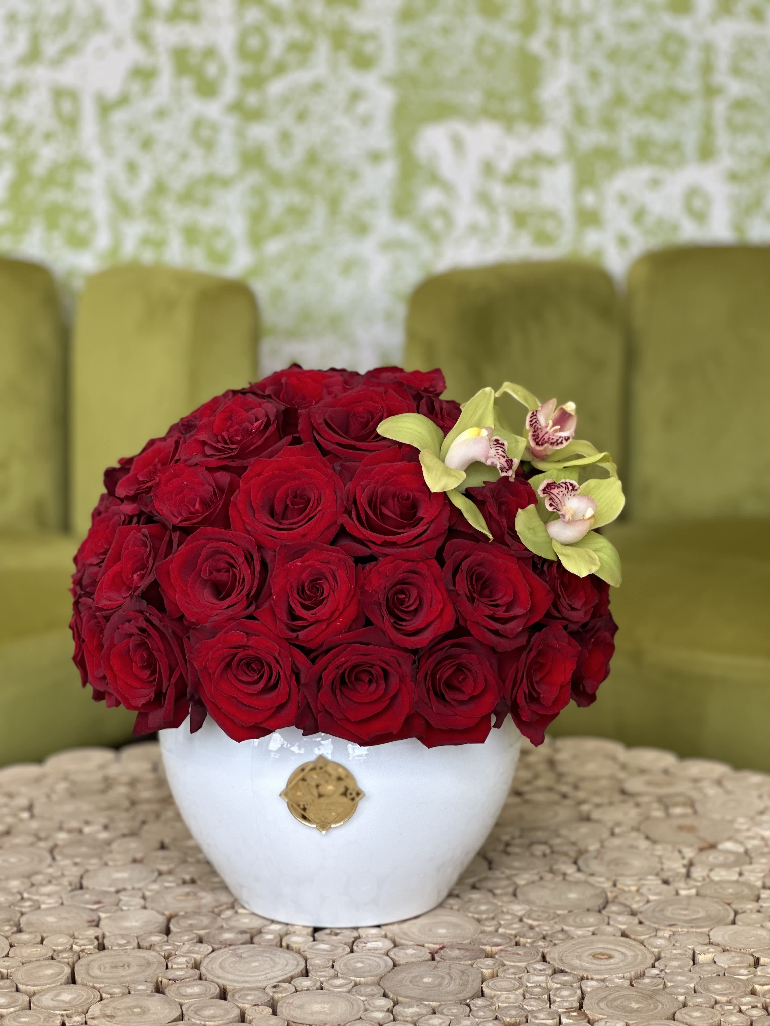 Red rose arrangement in a white vase with small orchid accents