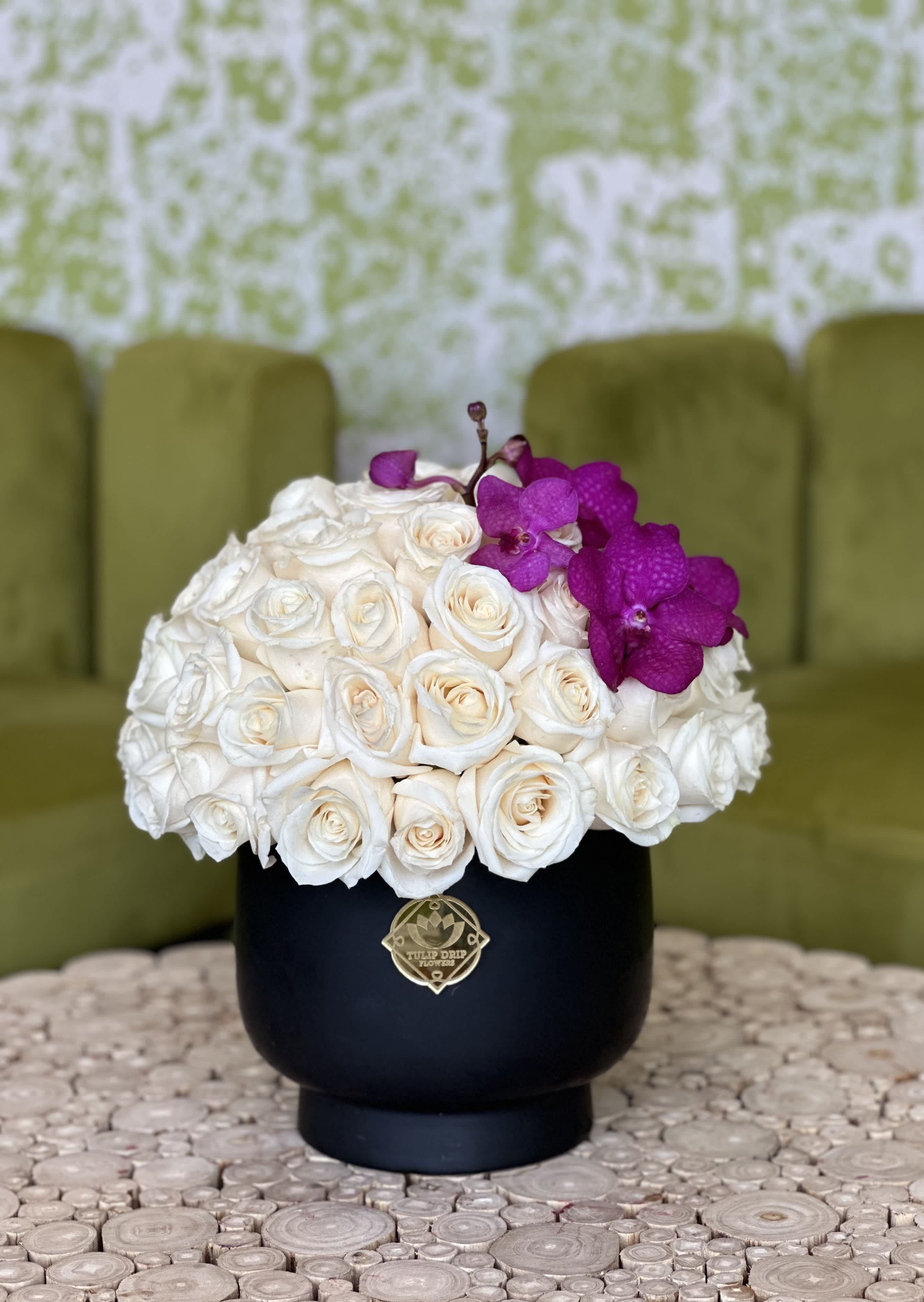 White rose arrangement with purple orchids in a black vase