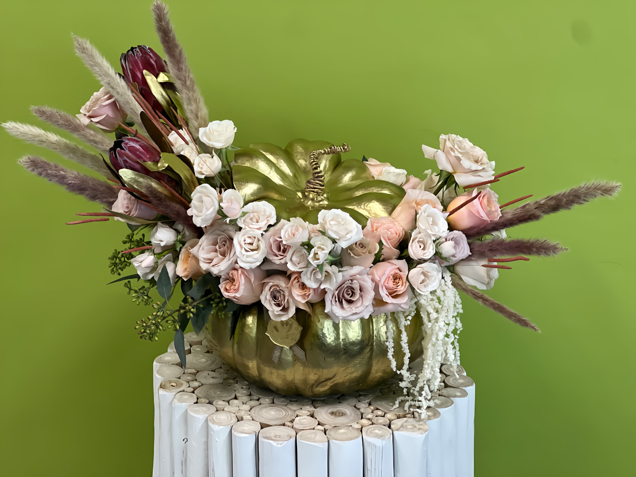 Floral arrangement in a gold pumpkin container with pale roses and burgundy blooms