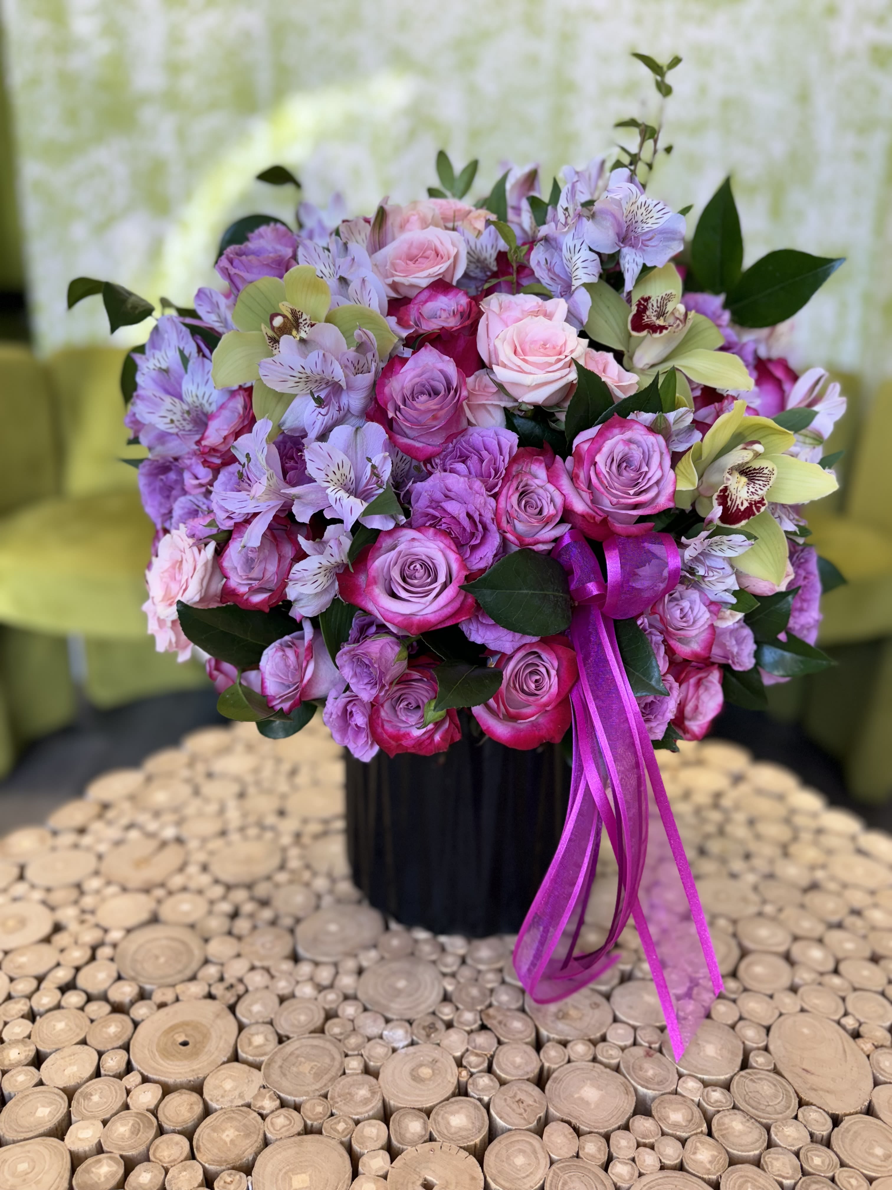 Pink and lavender bouquet of roses and orchids in a black vase with ribbon