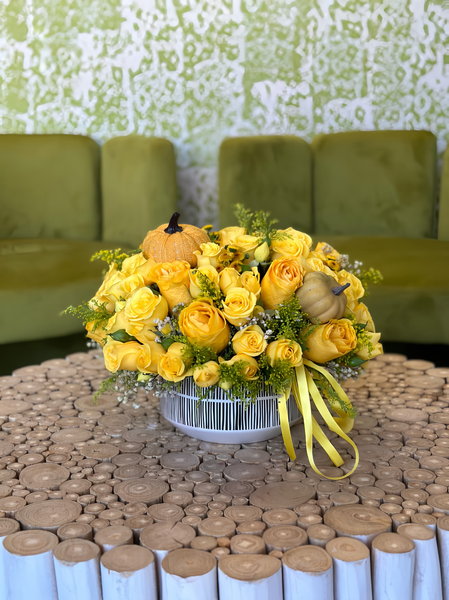 Yellow rose arrangement in a striped white container with small pumpkins