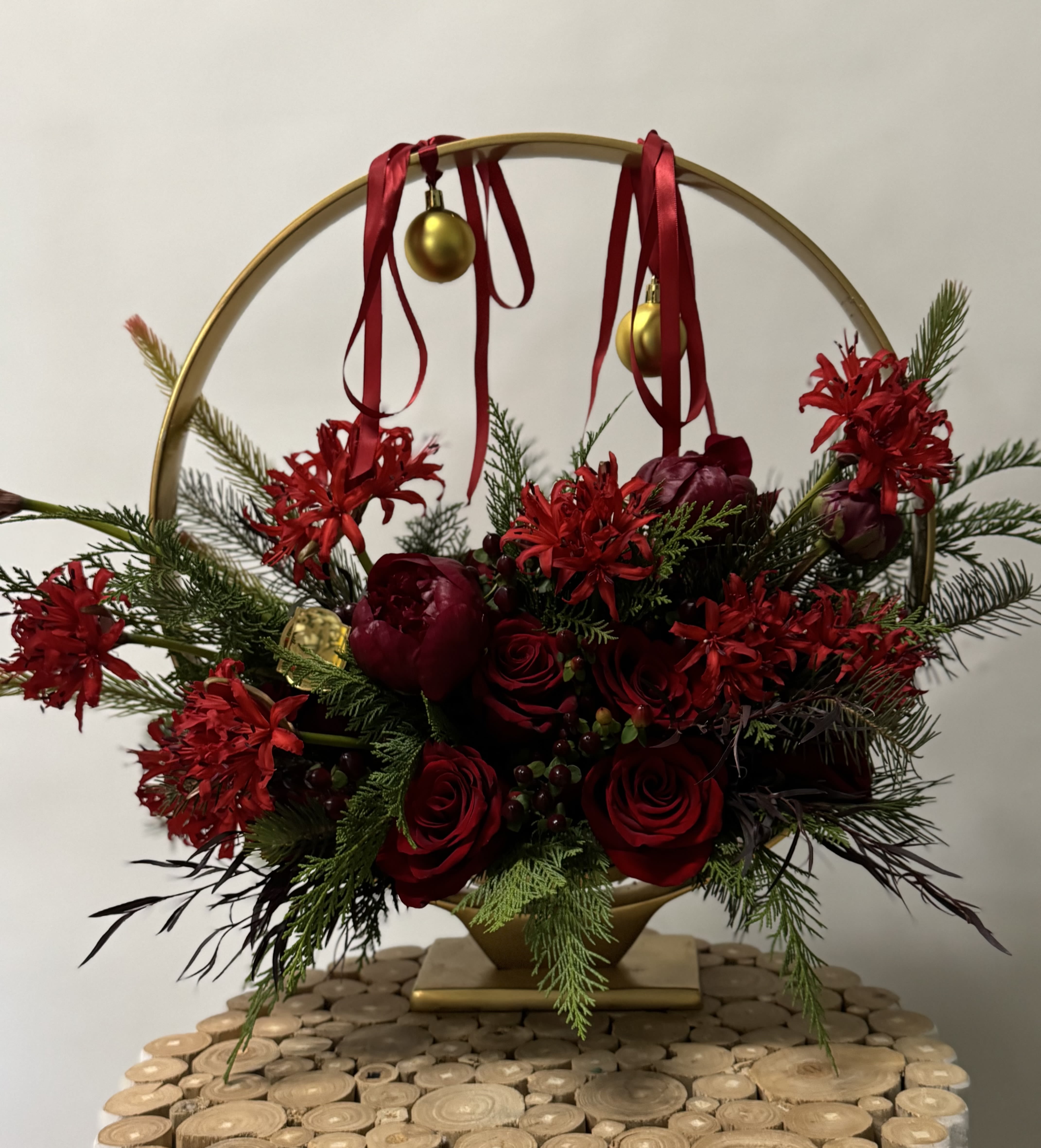Red roses and holiday flowers arranged in a gold hoop with ribbon and ornaments