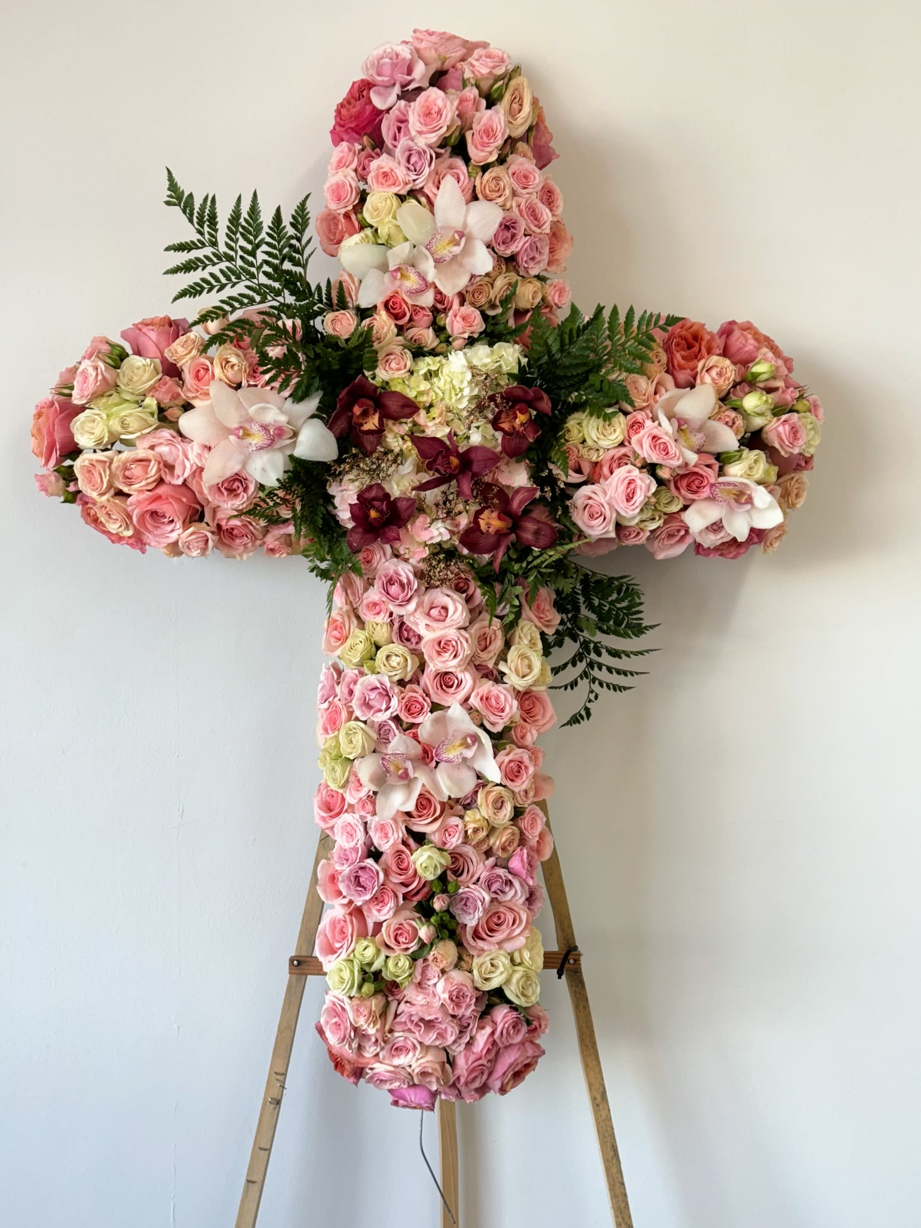 Large floral cross covered in pink roses and orchids on an easel