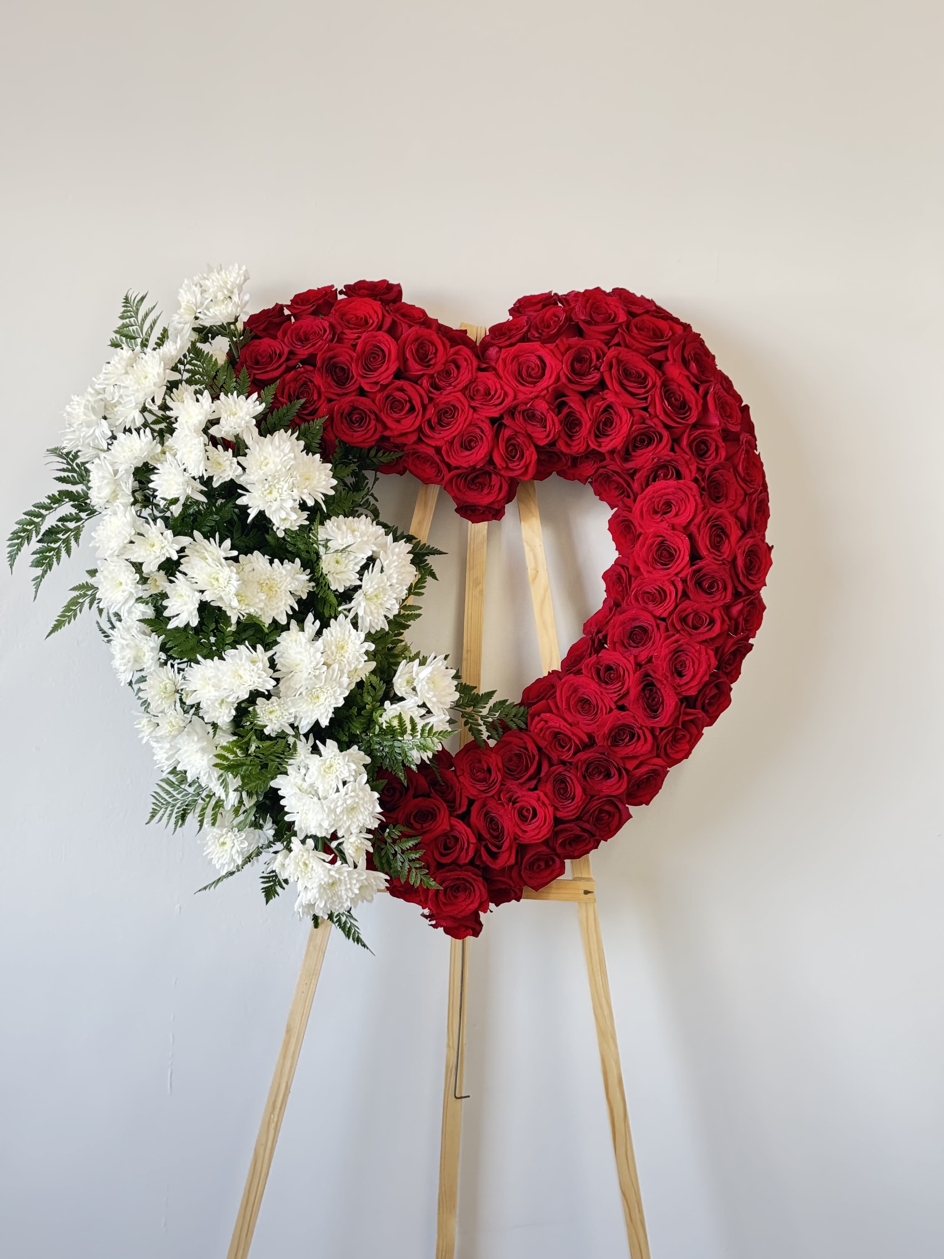 Heart-shaped floral wreath of red roses and white chrysanthemums on an easel