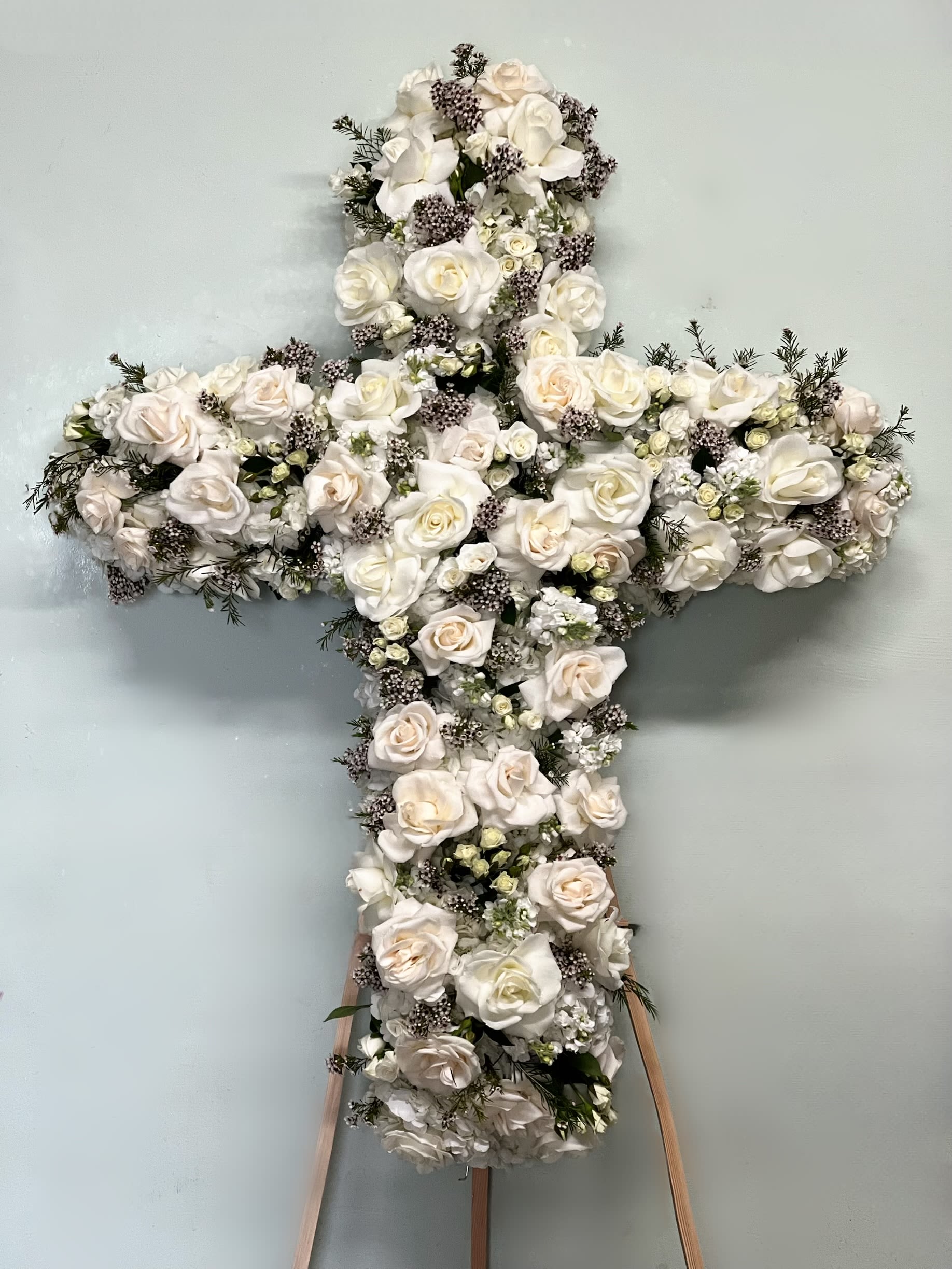 White floral cross arrangement with roses on a stand