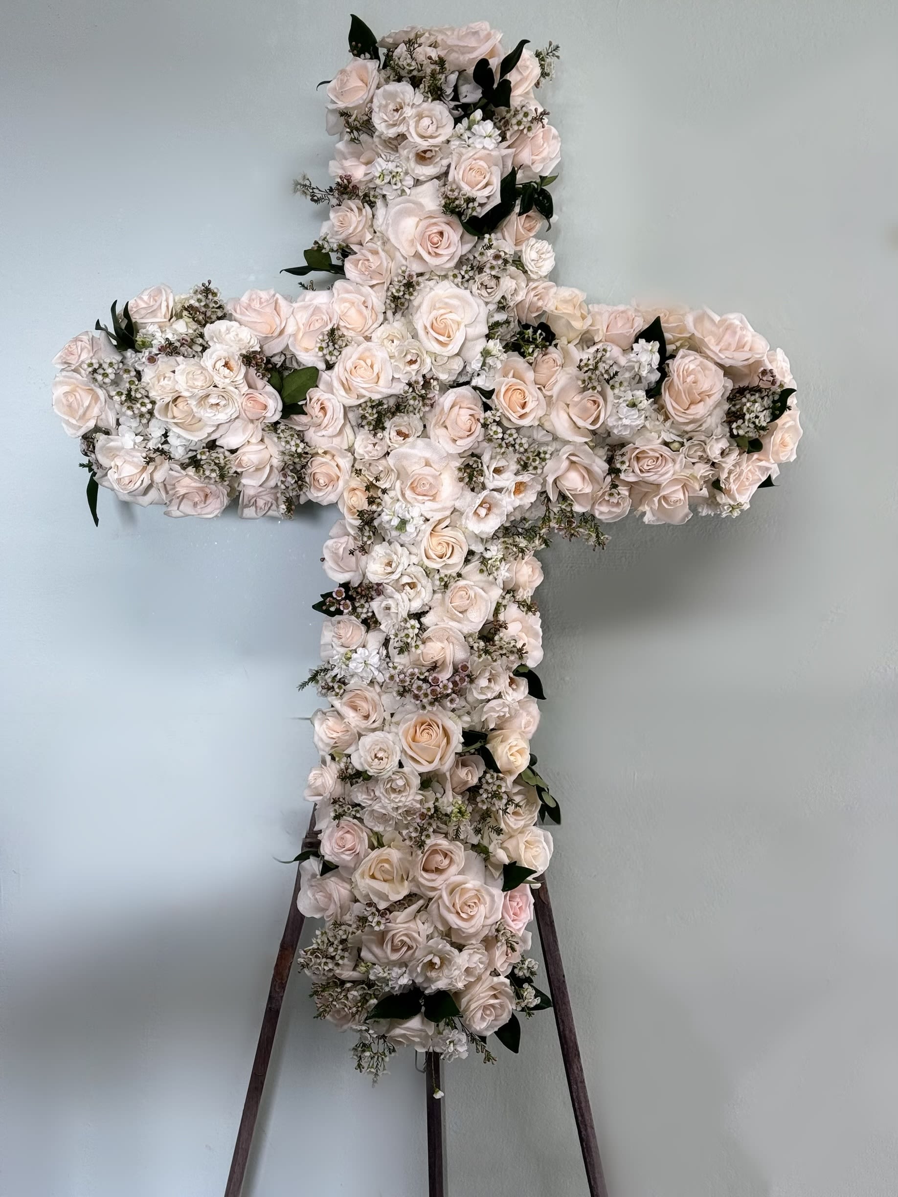 Cross-shaped floral arrangement of pale roses and white blooms on a stand