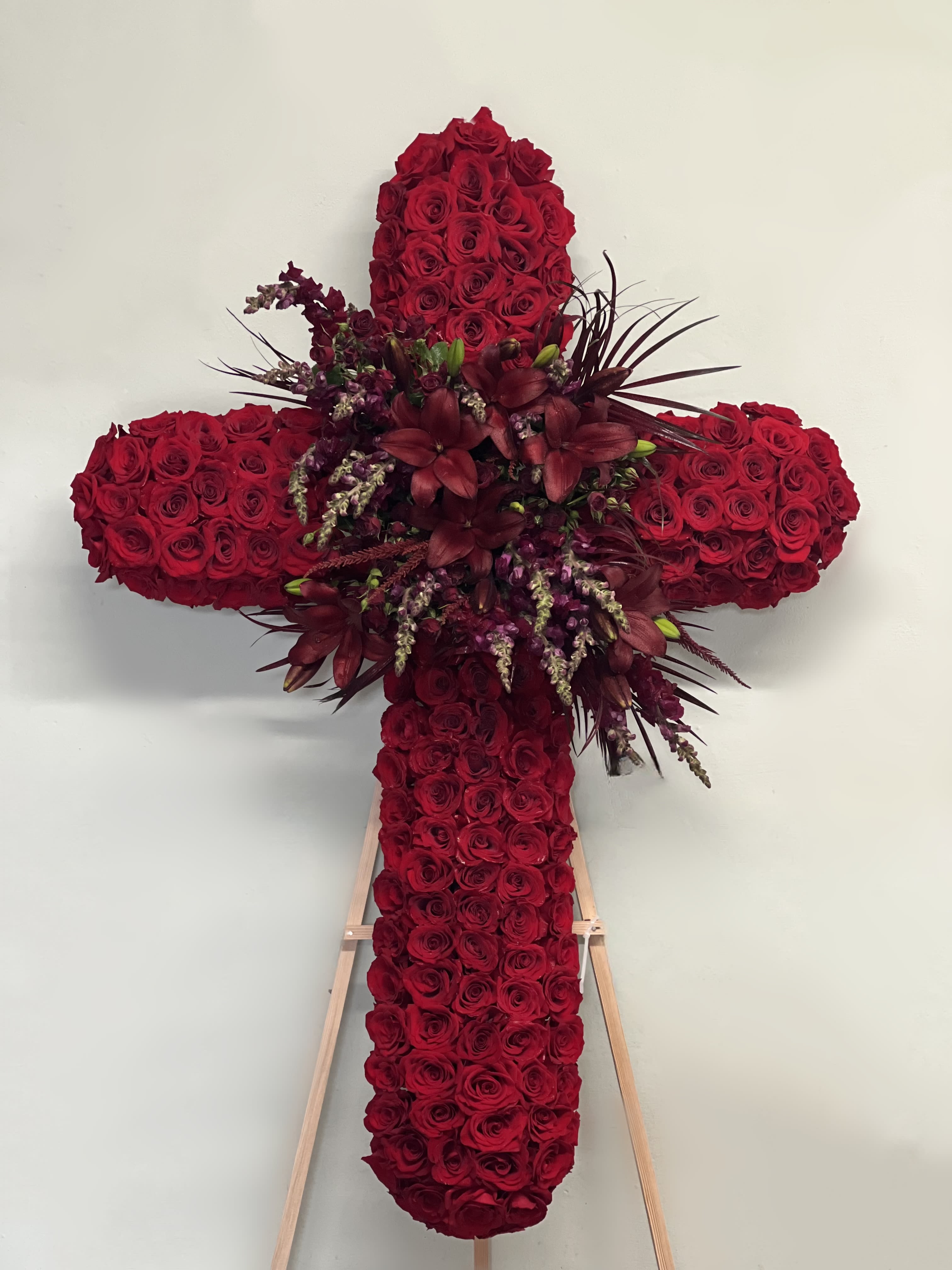 Cross-shaped floral tribute made of red roses with dark accent flowers