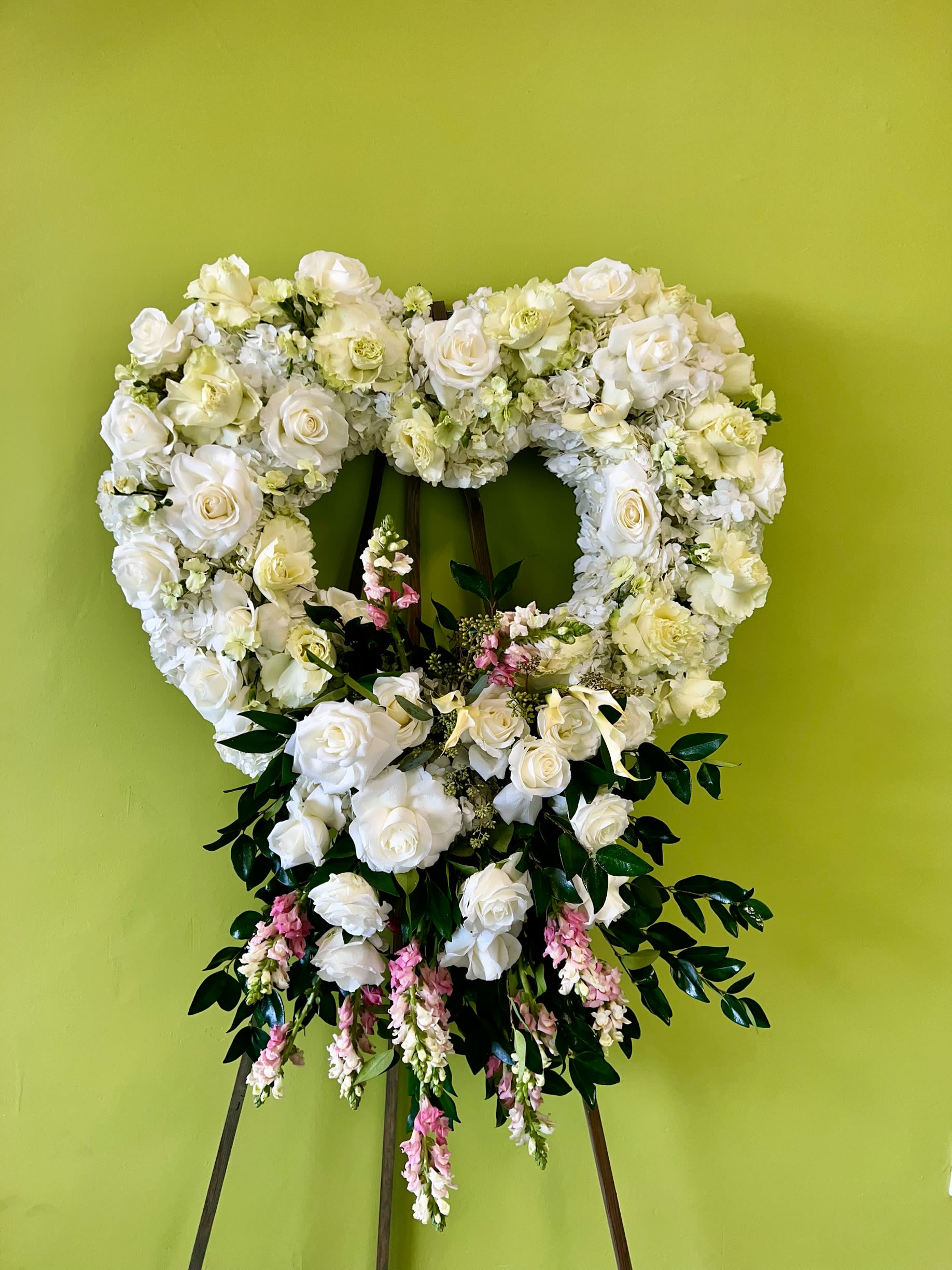 Heart-shaped white floral wreath on an easel with pink accents