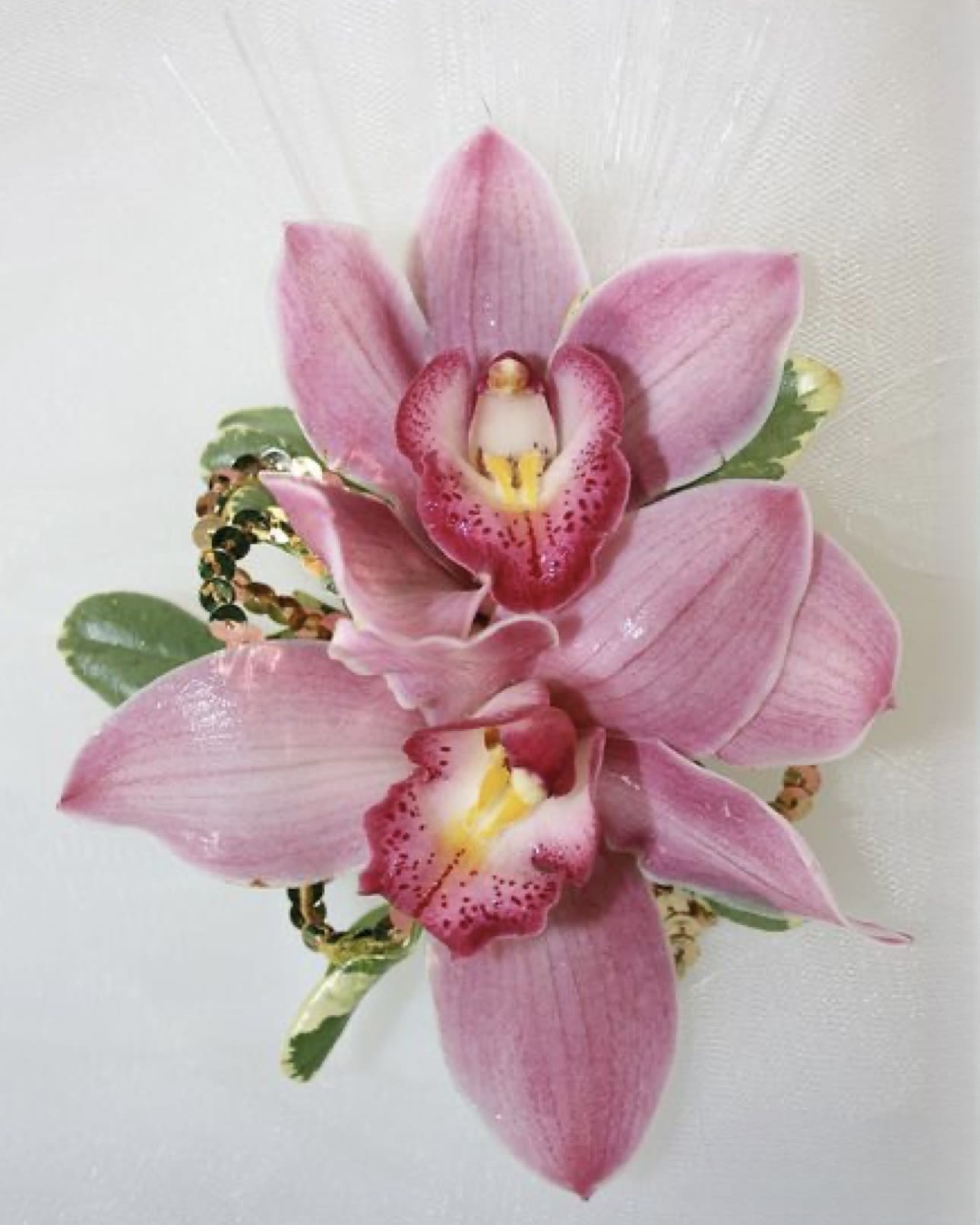 Pink orchid corsage with sequined accents on a white background