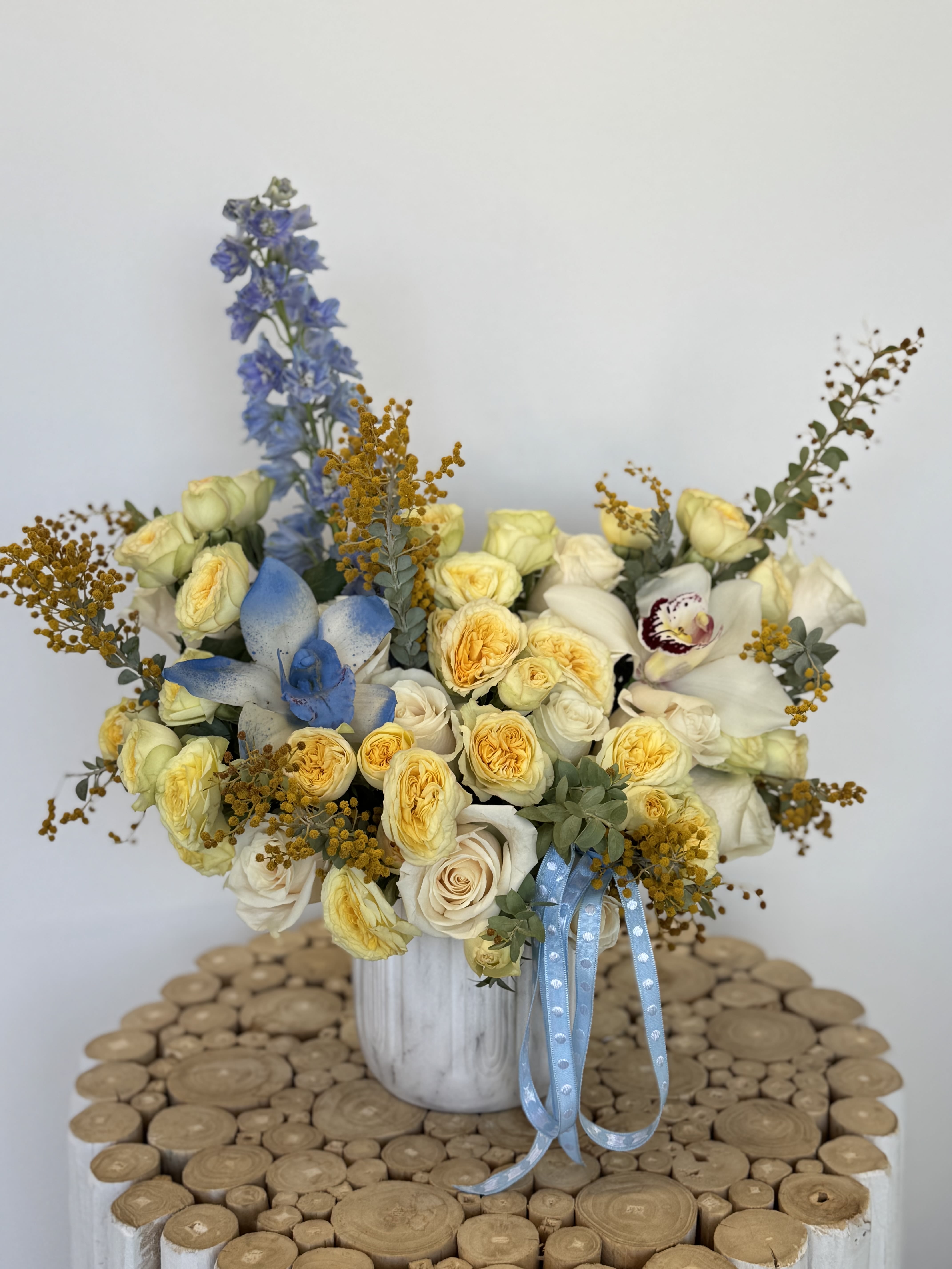 Bouquet of pale yellow and white roses in a white vase with blue ribbon