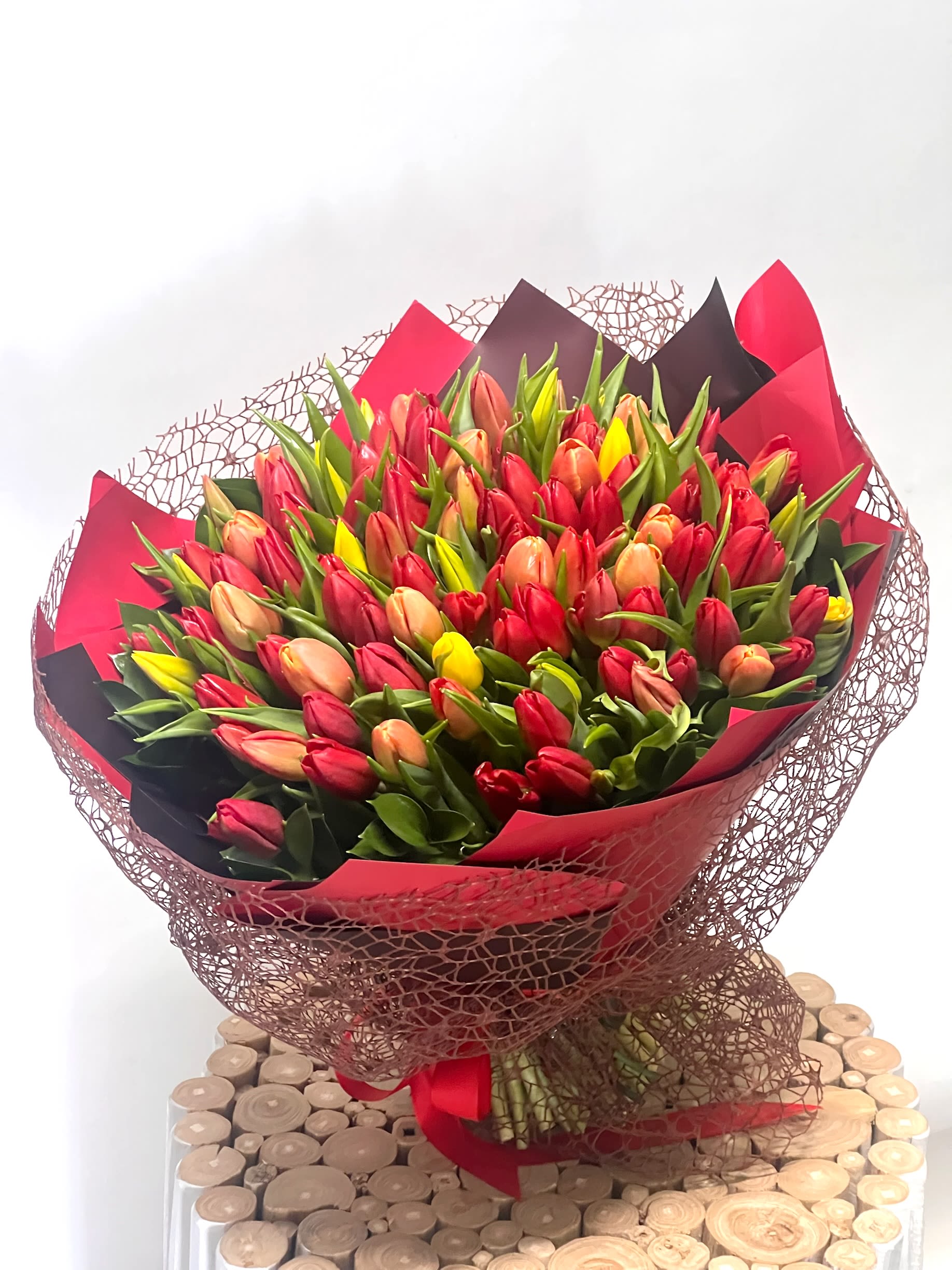 Large bouquet of red, pink, peach, and yellow tulips wrapped in red and black paper