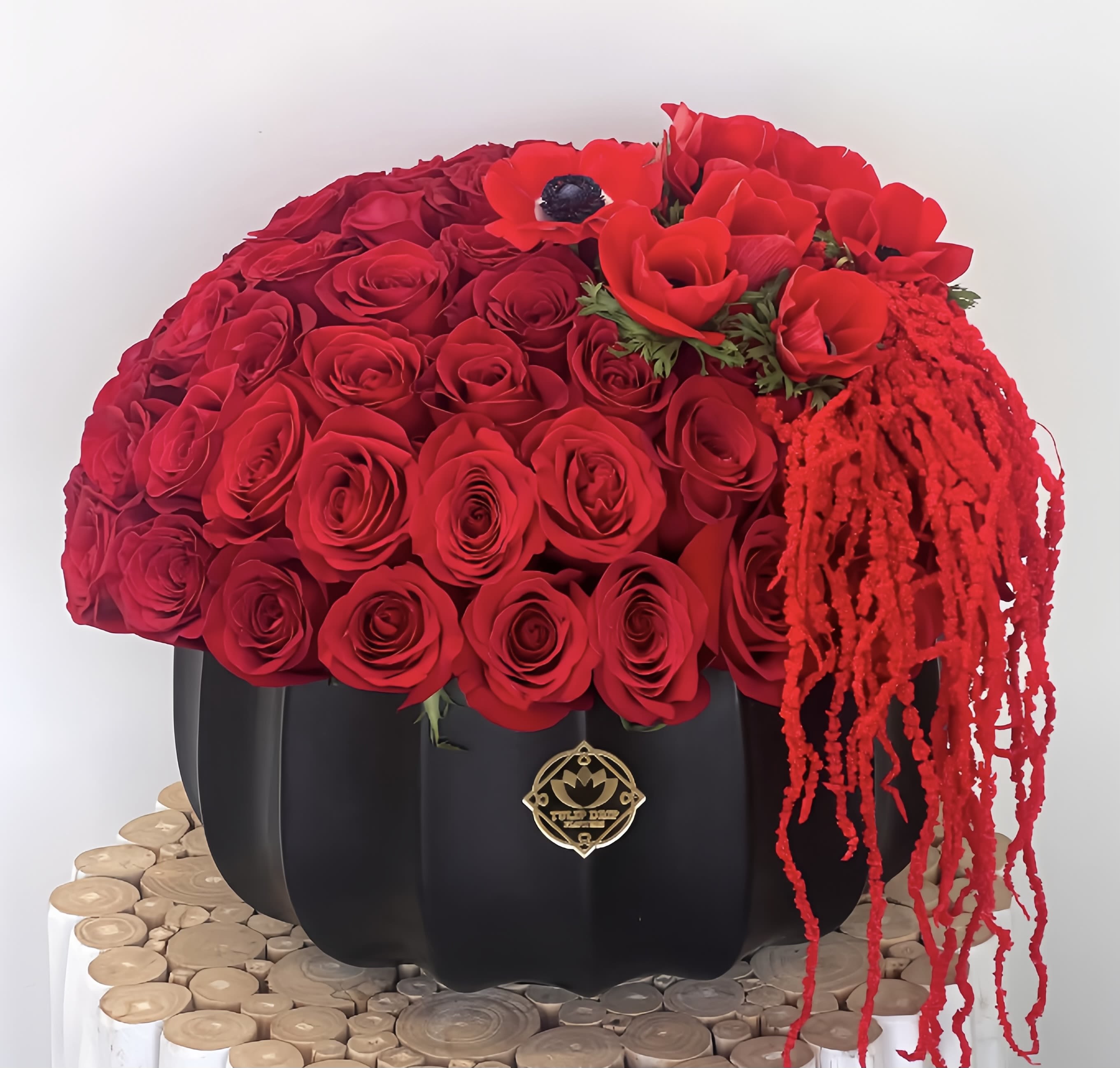 Red rose arrangement in a black pumpkin-shaped container with trailing red accents