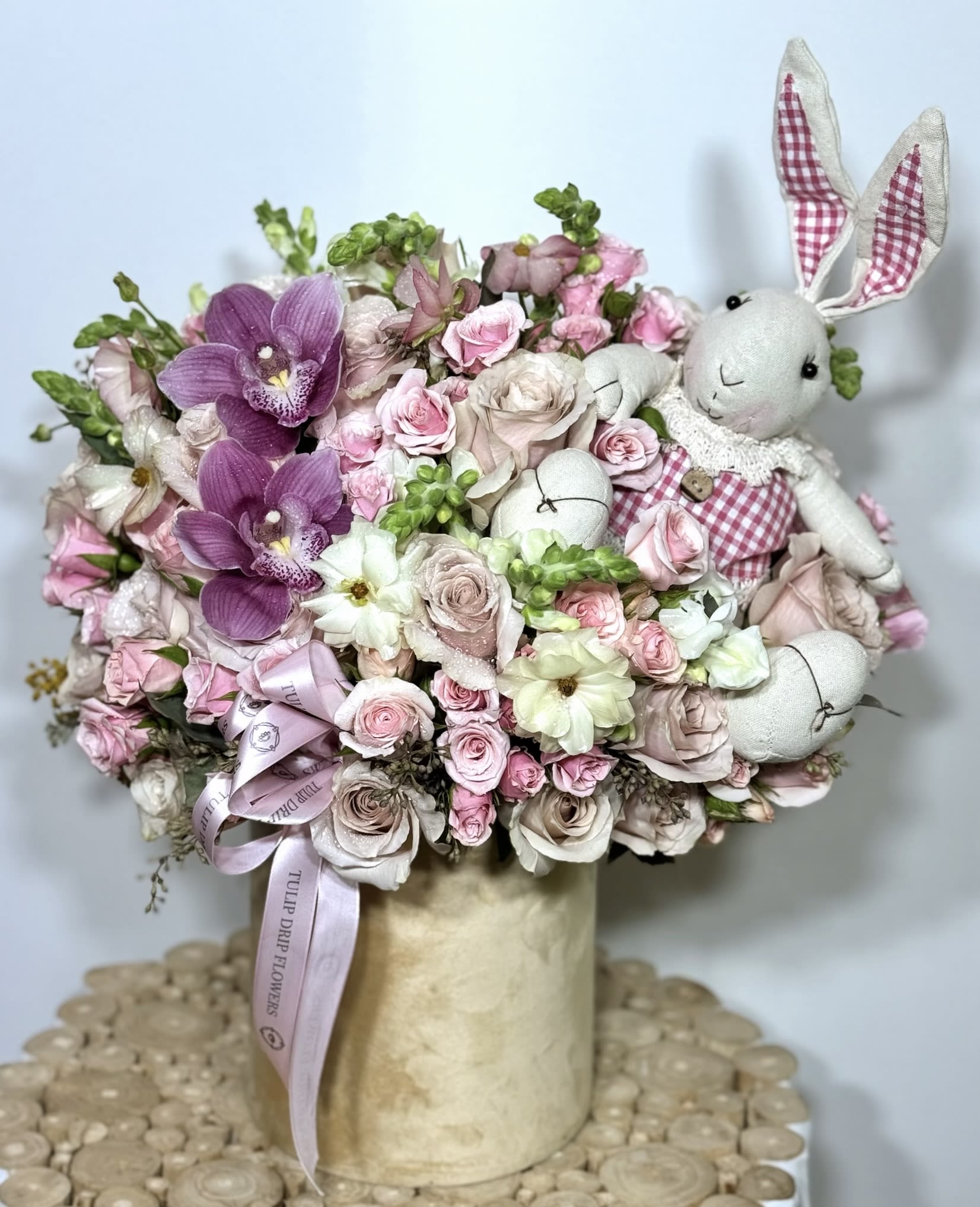 Pink and white floral arrangement with plush bunny figures in a vase