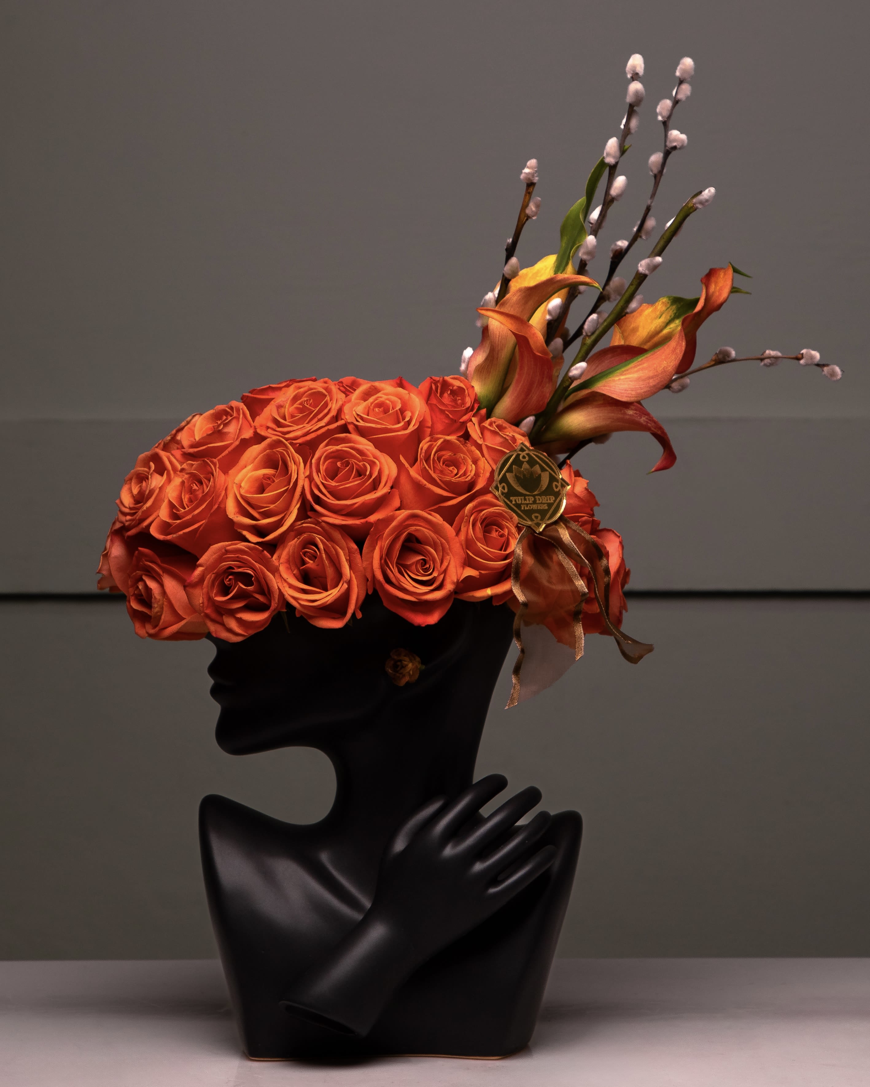 Orange rose arrangement in a black bust vase with pussy willow stems