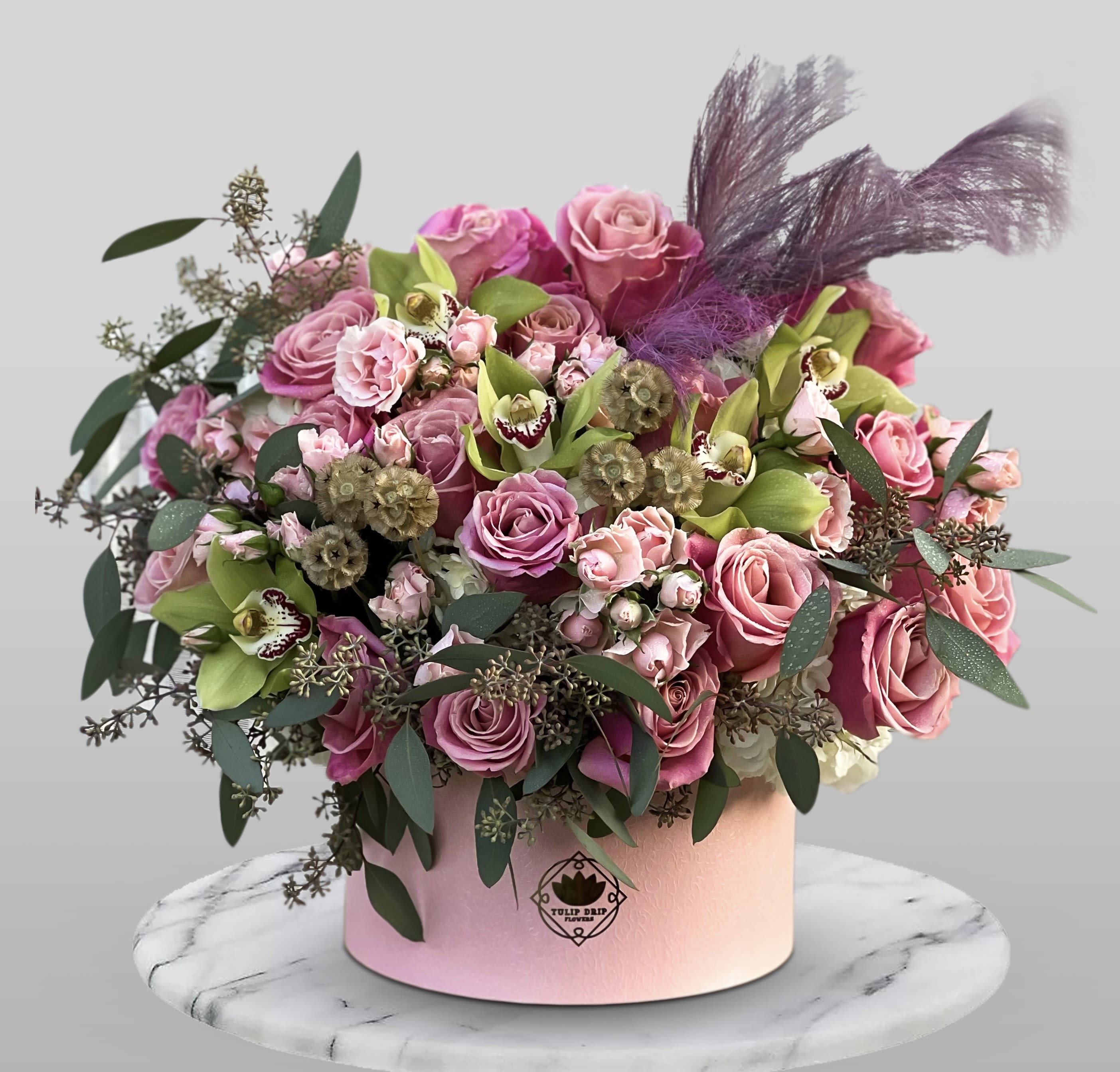 Pink rose bouquet in a round pink box with purple feathers