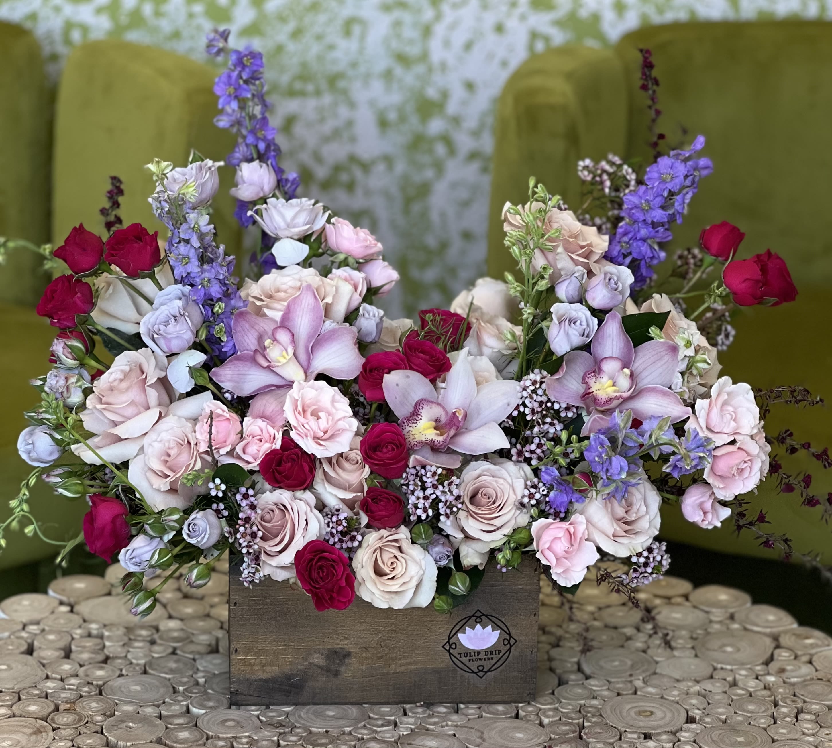 Mixed bouquet of roses, orchids, and purple blooms in a wooden box
