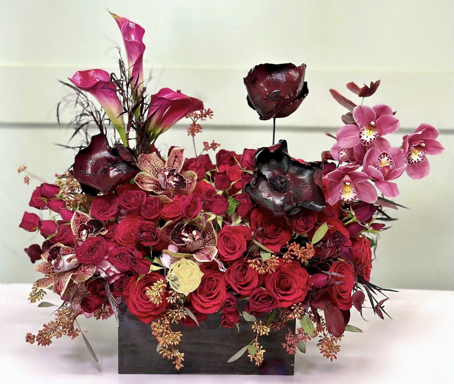 Red rose arrangement with pink orchids in a black rectangular vase