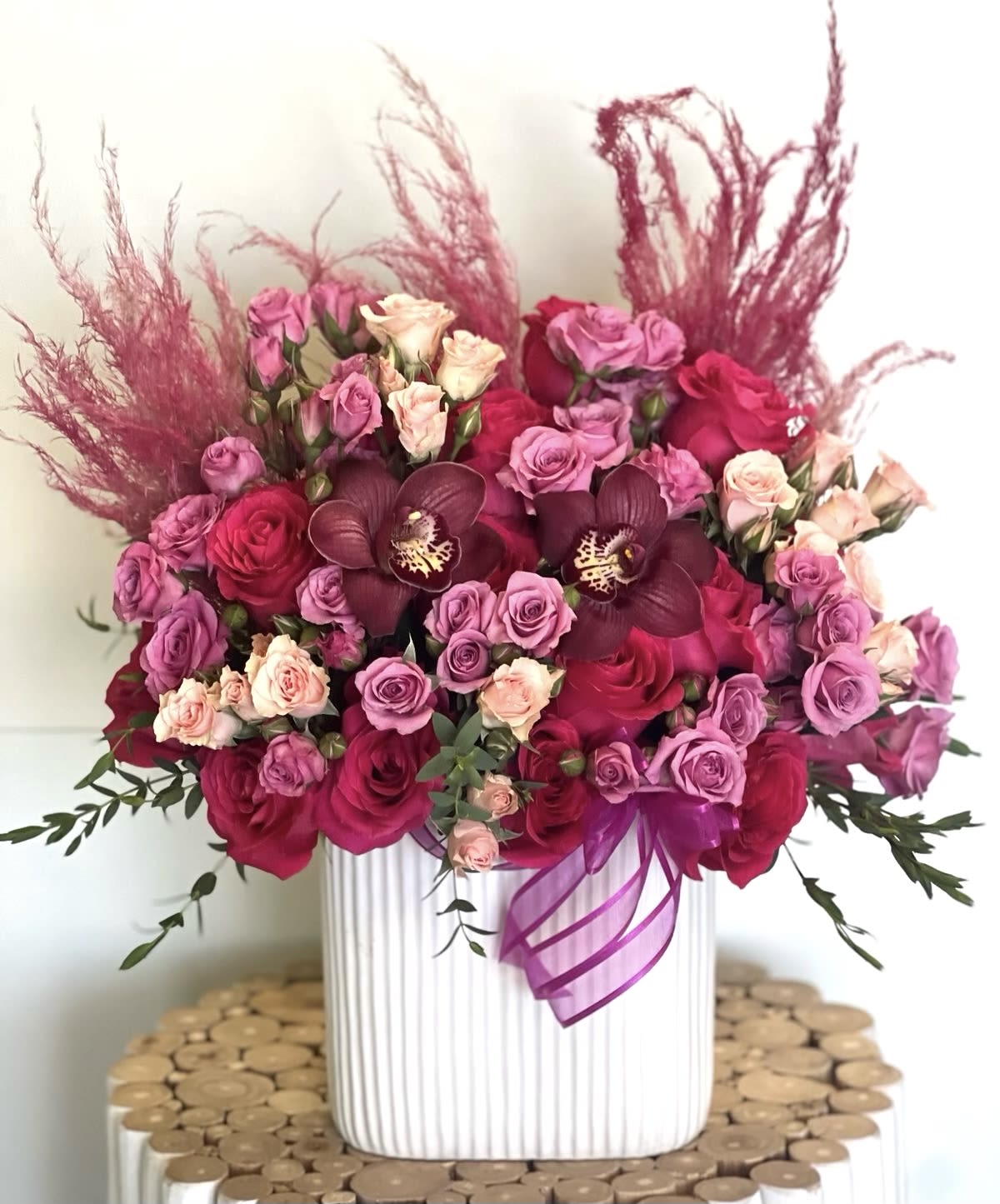 Pink and red rose arrangement in a white vase with a purple ribbon