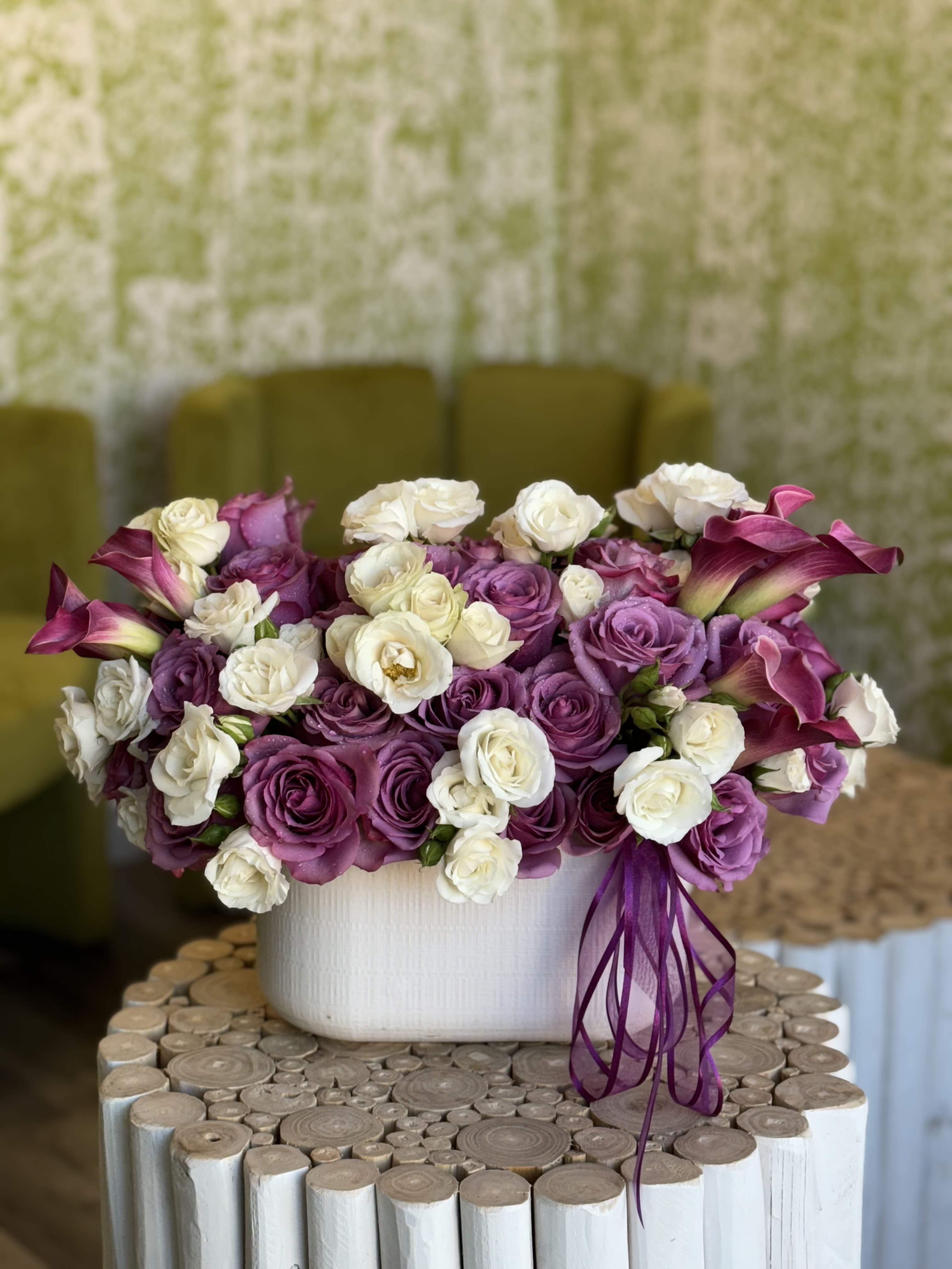 Purple and white rose arrangement in a white vase with calla lilies