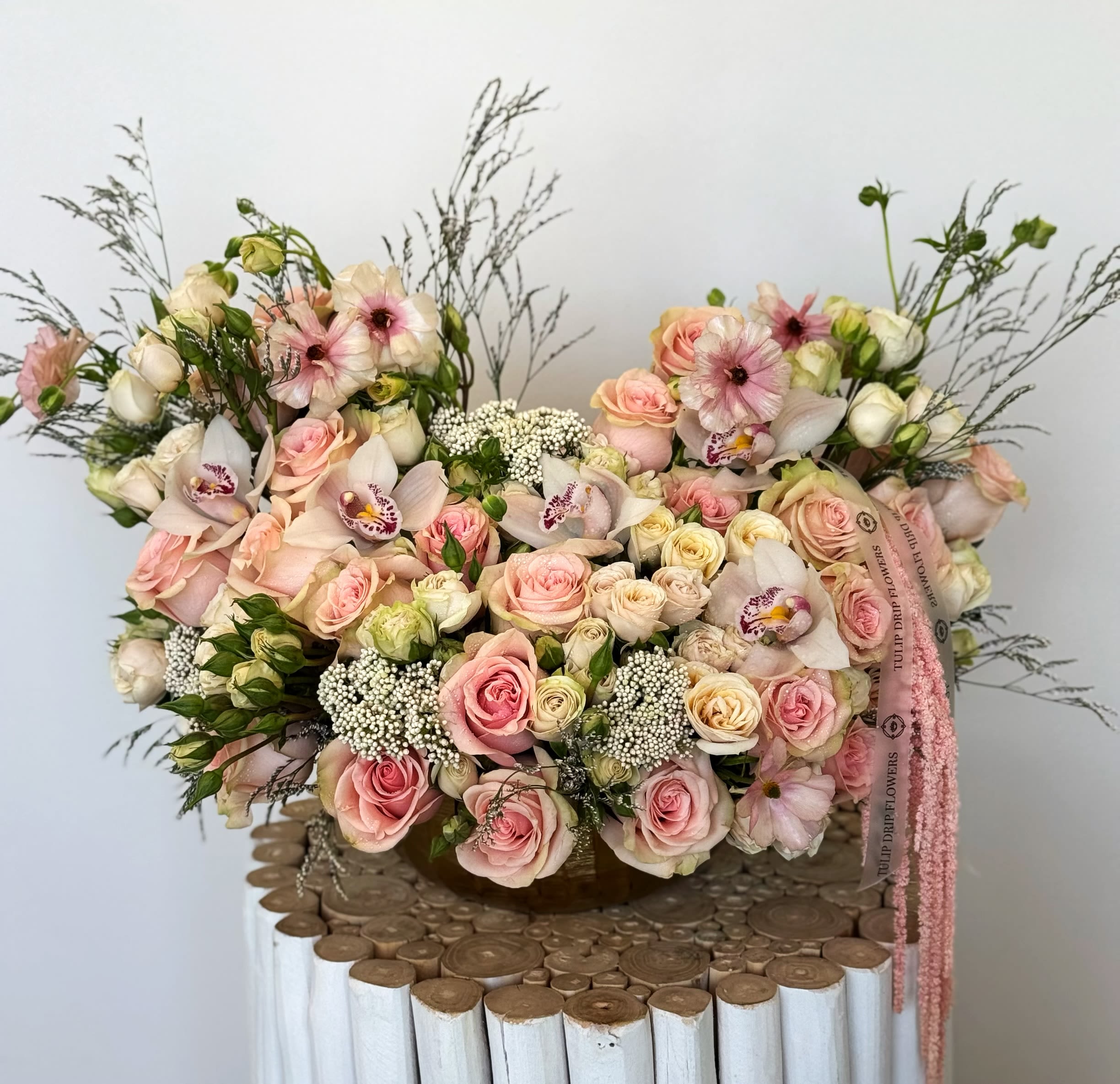 Large pastel bouquet of pink and cream roses with orchids in a basket