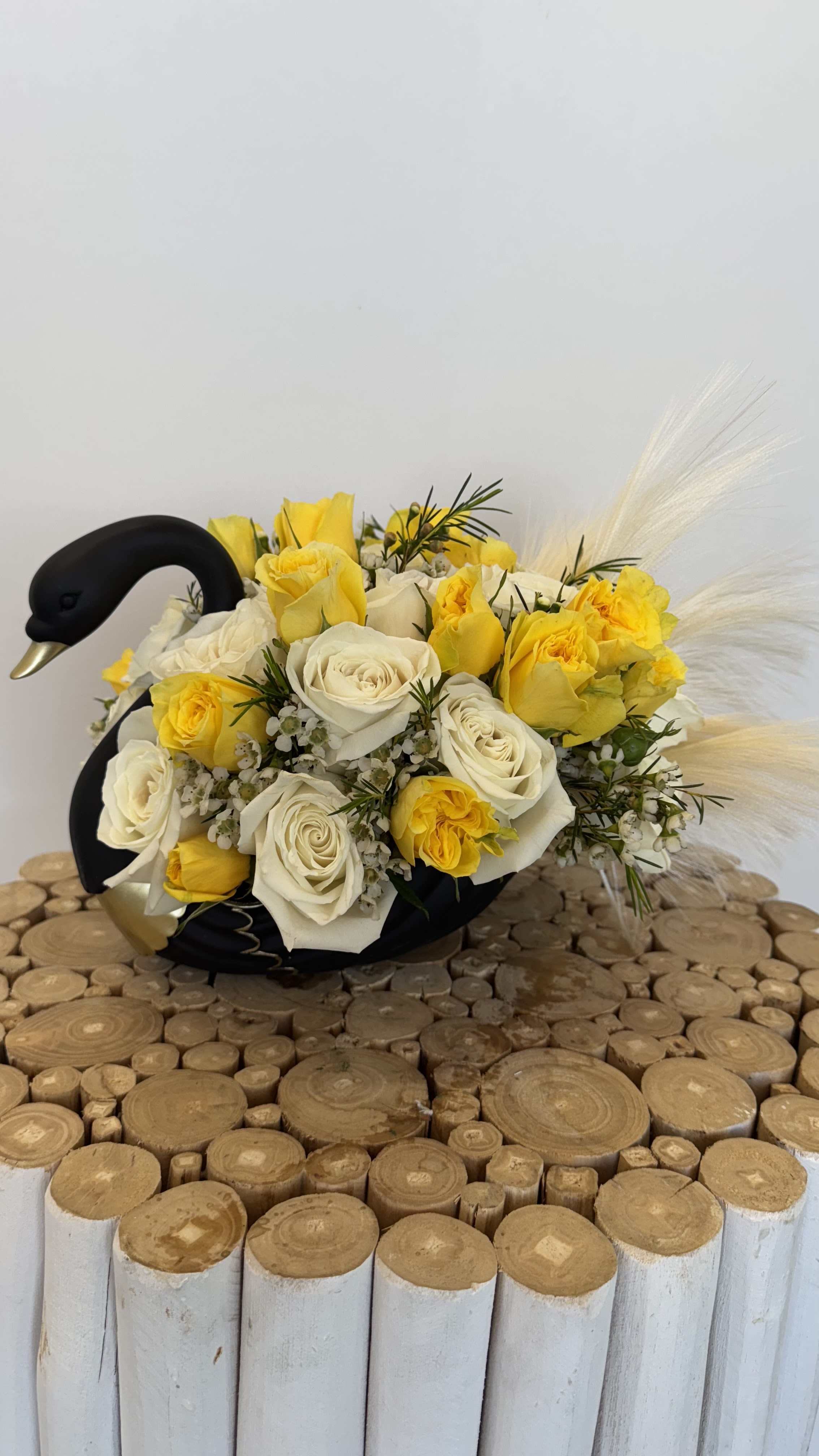 Yellow and white rose arrangement in a black swan-shaped container