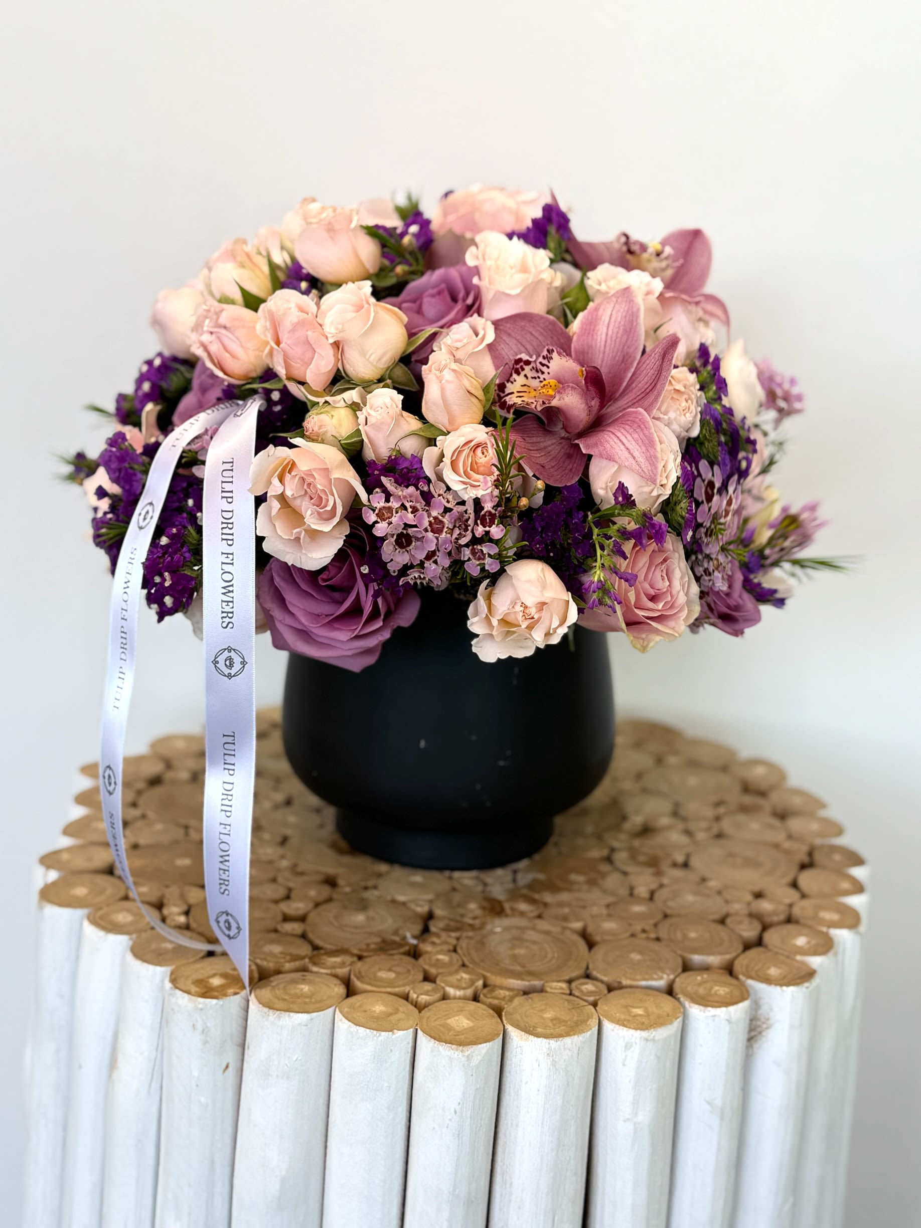 Pink and purple bouquet in a black vase with a ribbon
