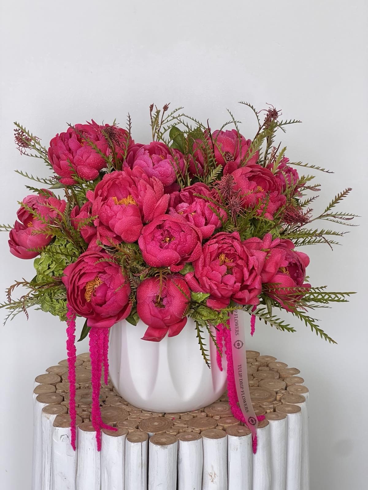 Bright pink bouquet in a white vase on a wooden stand
