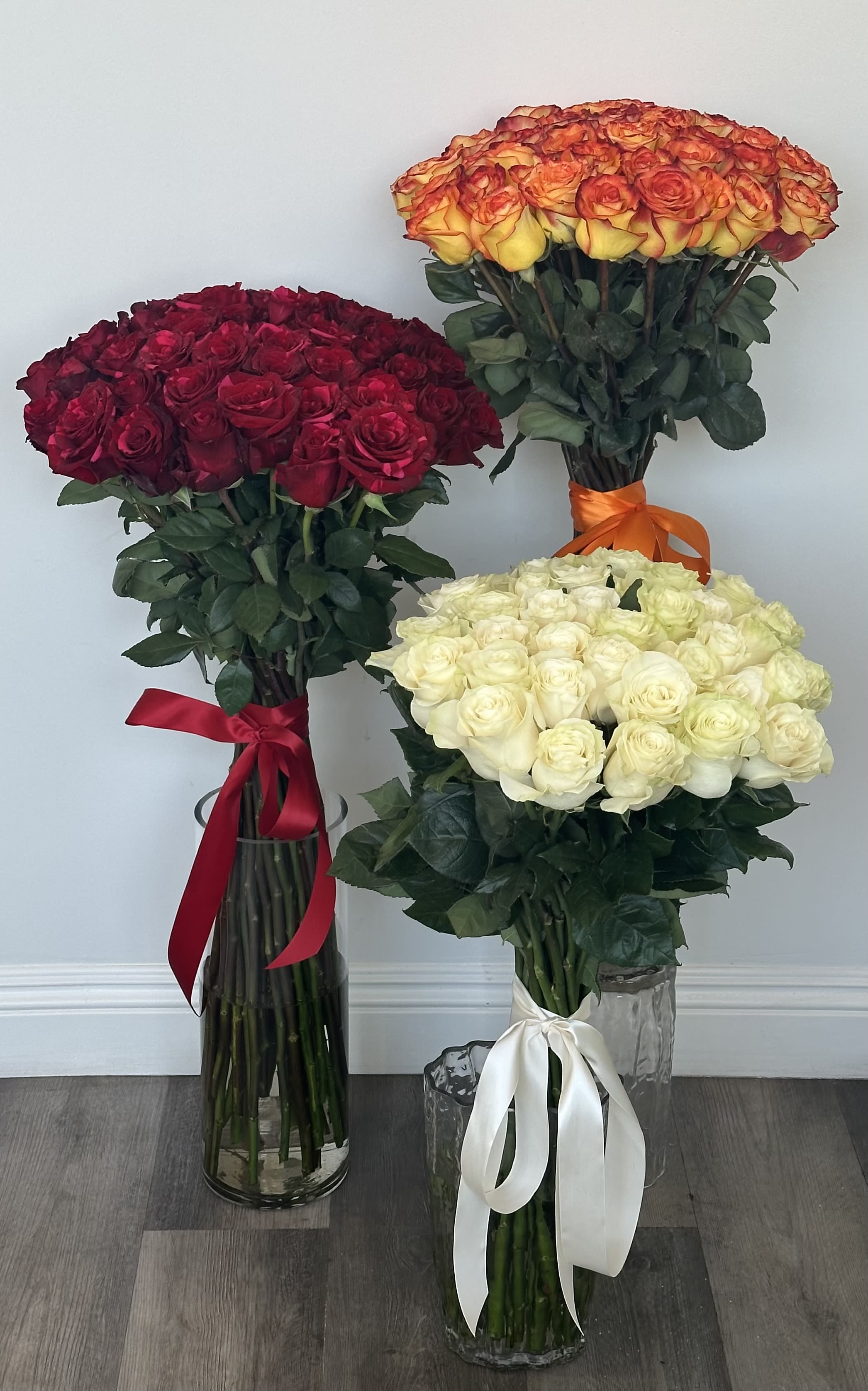 Three large rose bouquets in glass vases, in red, orange-yellow, and white