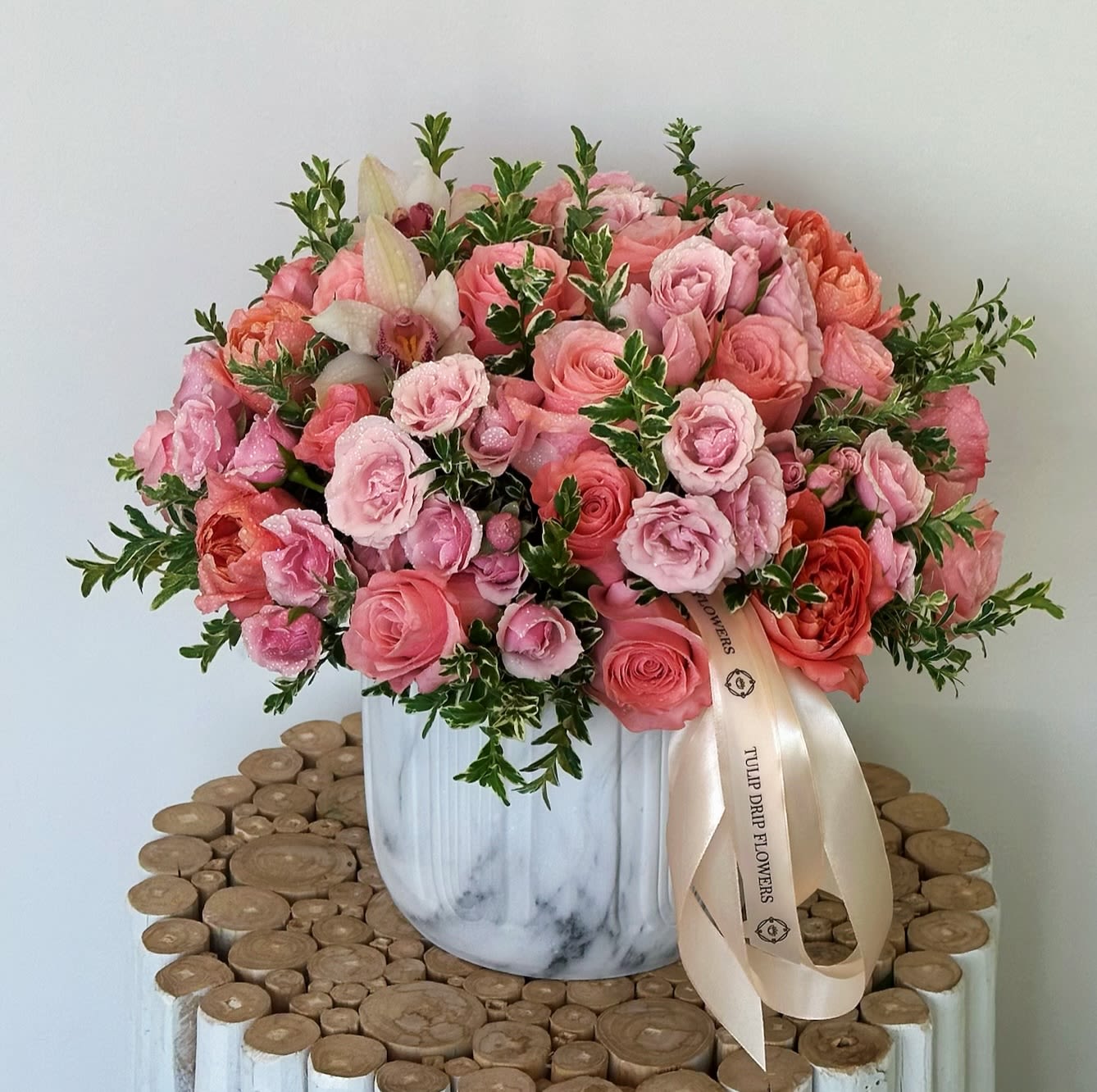 Pink and coral roses arranged in a white vase with a ribbon
