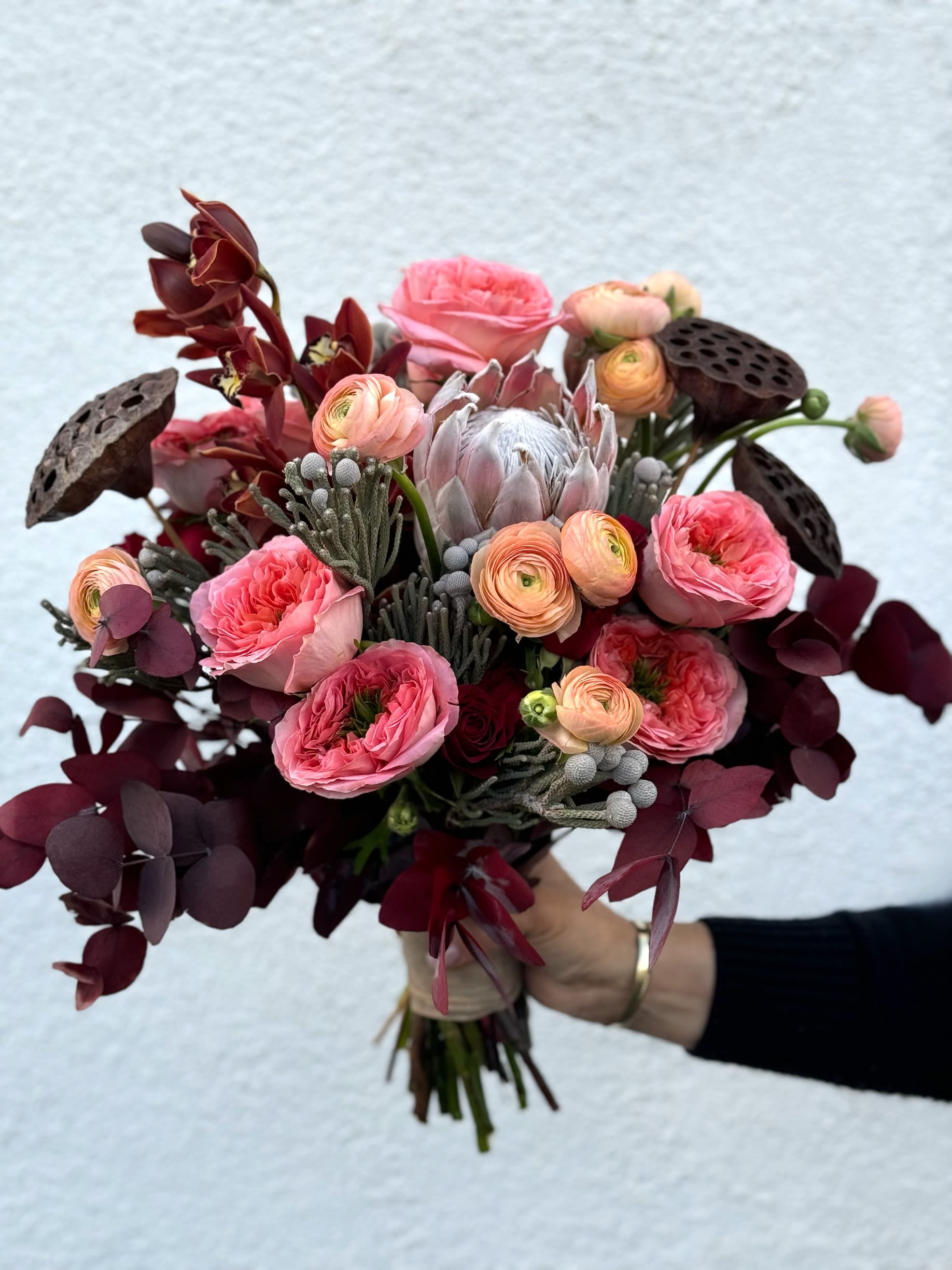 Handheld bouquet of pink and burgundy flowers with dark foliage