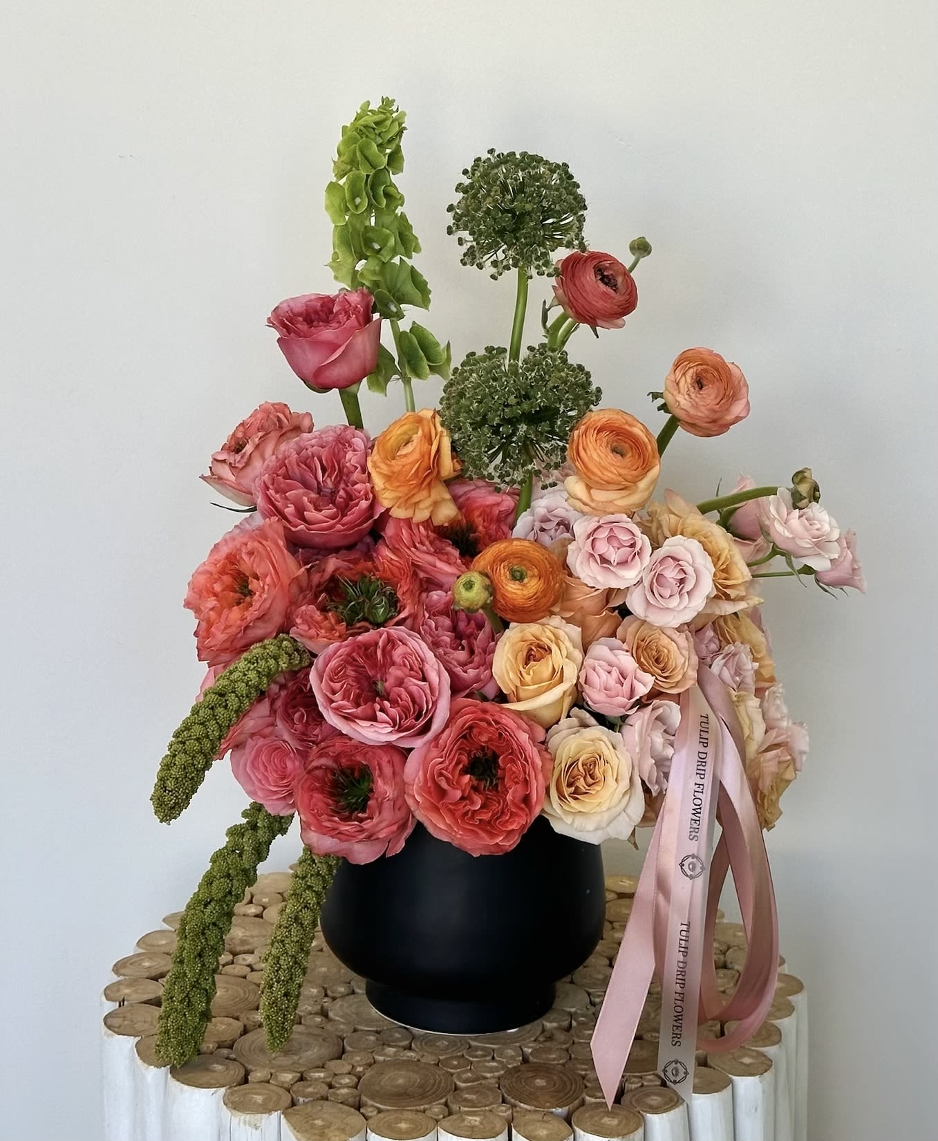 Mixed bouquet of pink, peach, and orange flowers in a black vase