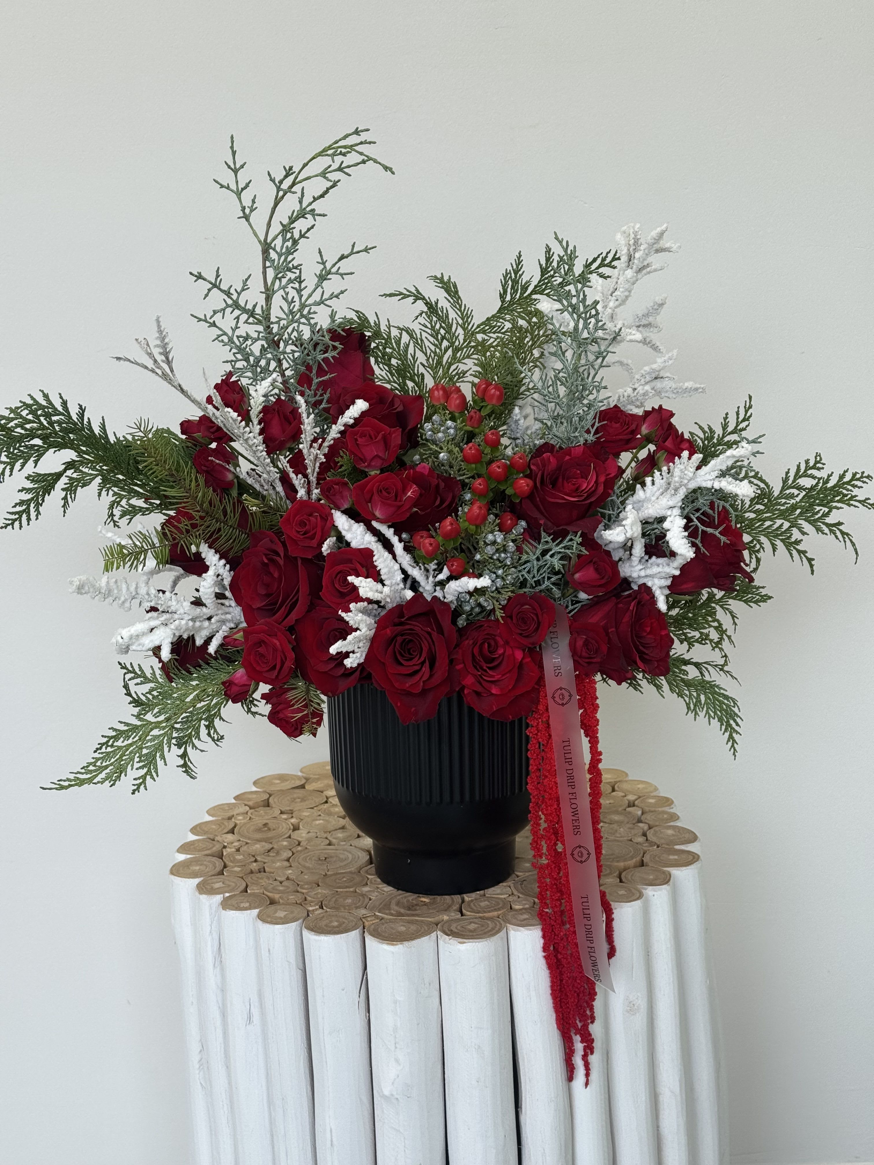 Red rose arrangement in a black vase with white frosted accents