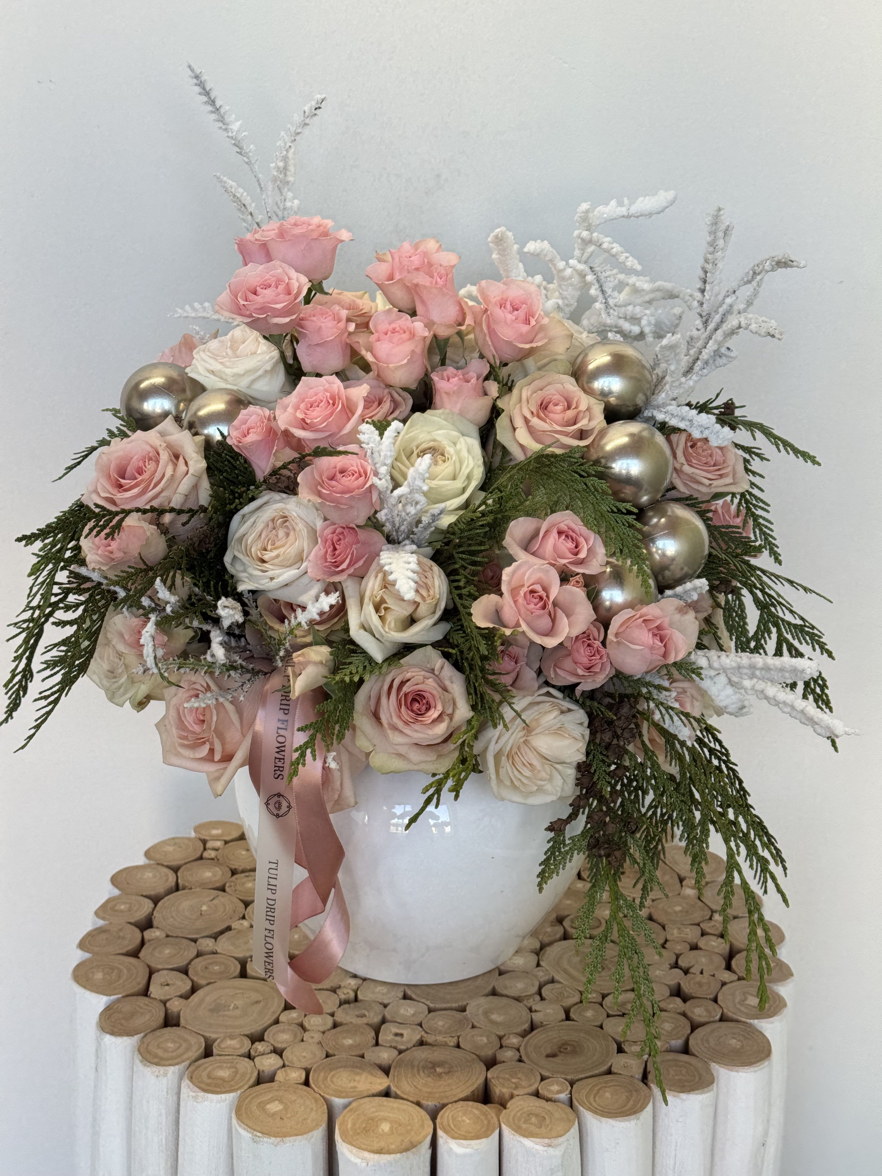 Pink and white roses arranged in a white vase with silver ornaments